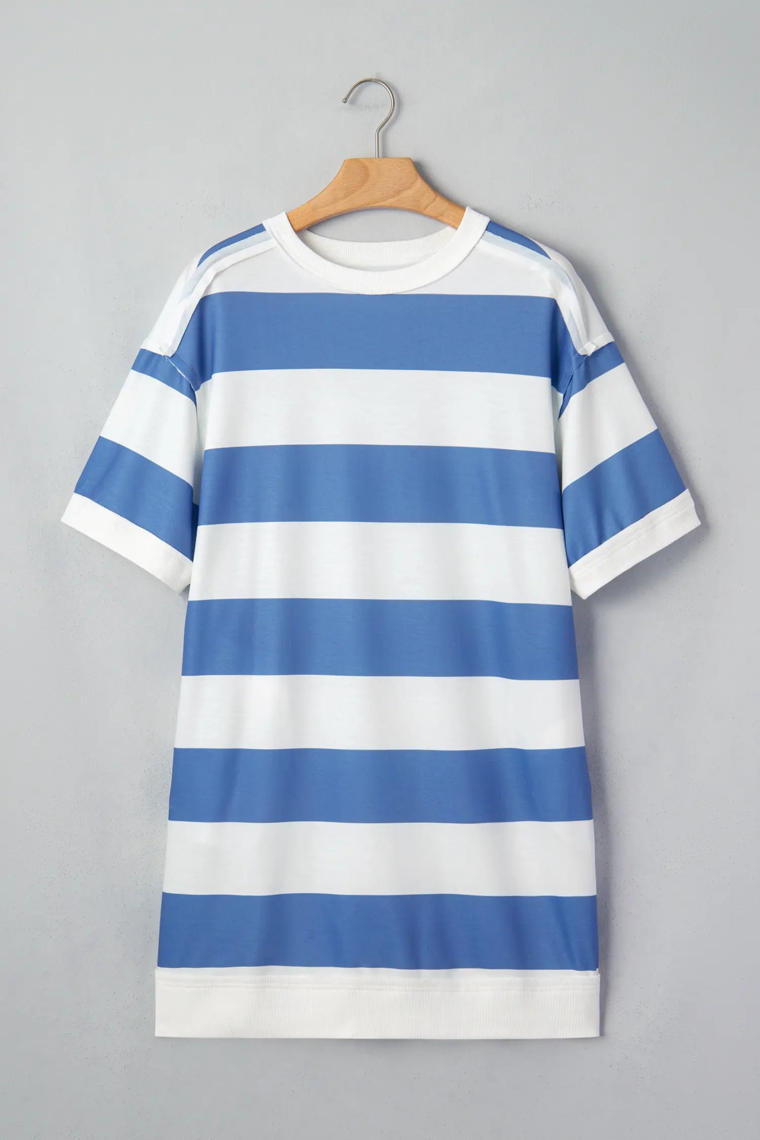 A short-sleeve crewneck T-shirt dress with horizontal blue and white stripes, hanging on a wooden hanger against a solid gray background.