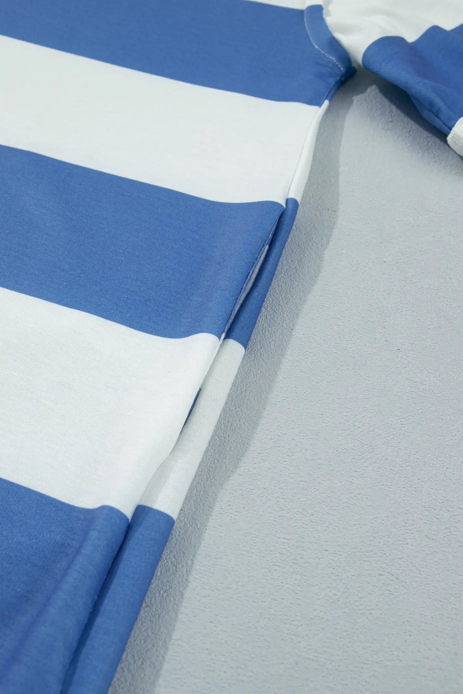 A close-up of a blue and white striped garment laid flat on a light gray textured surface.