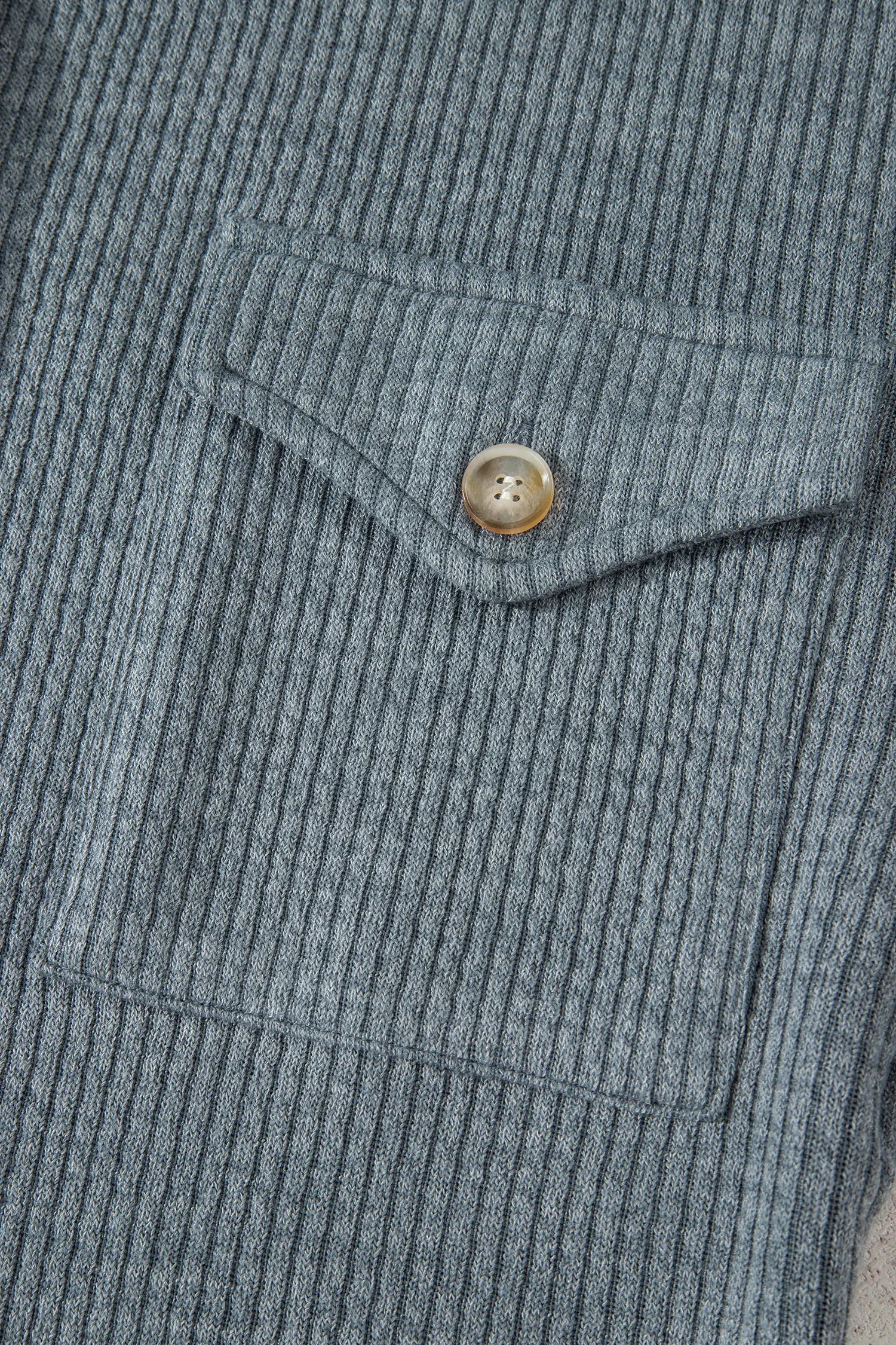 Close-up of a ribbed fabric pocket with a button on a gray textured background