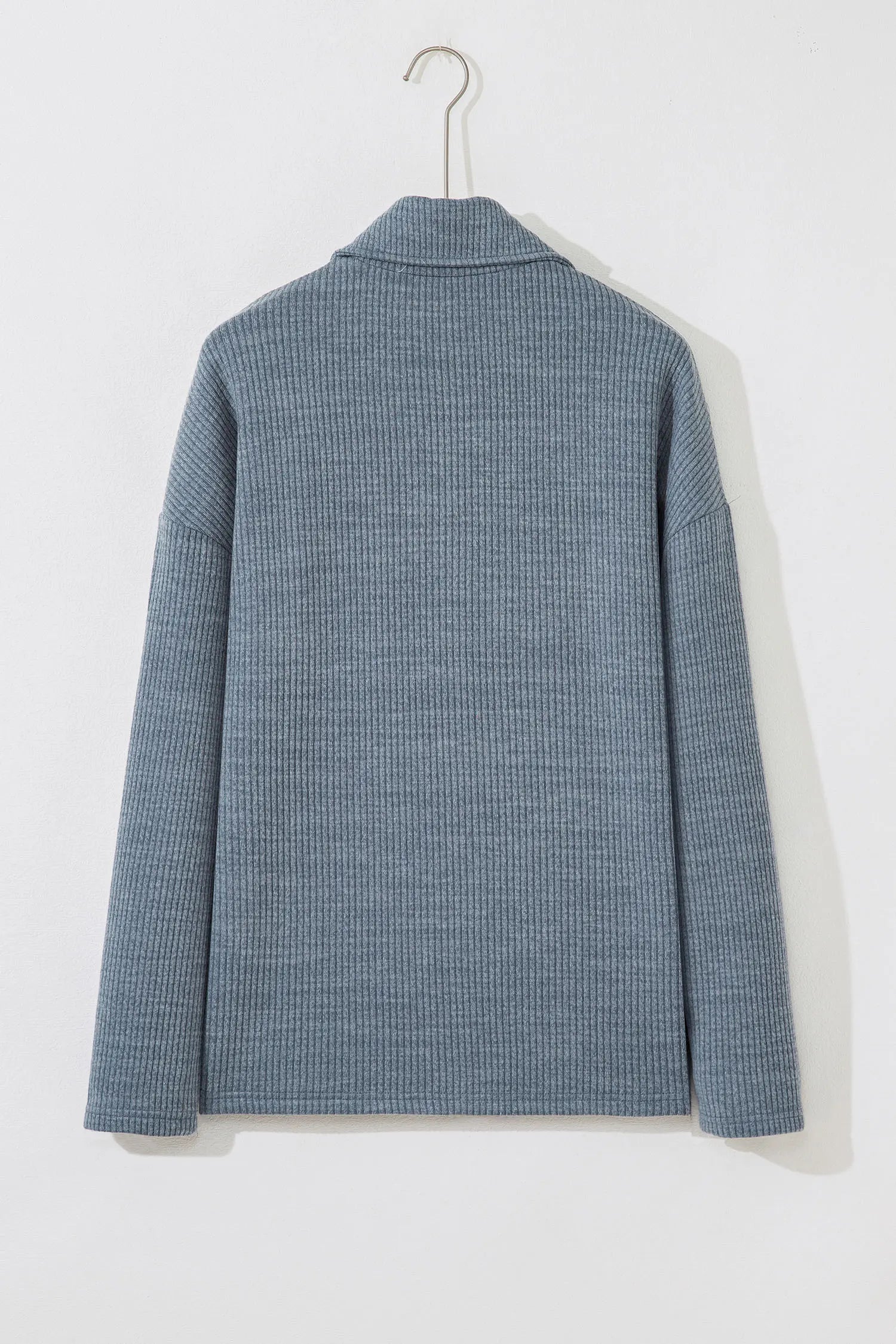 A textured blue-gray ribbed knit sweater with a mock neck, shown from the back on a white hanger against a white wall.