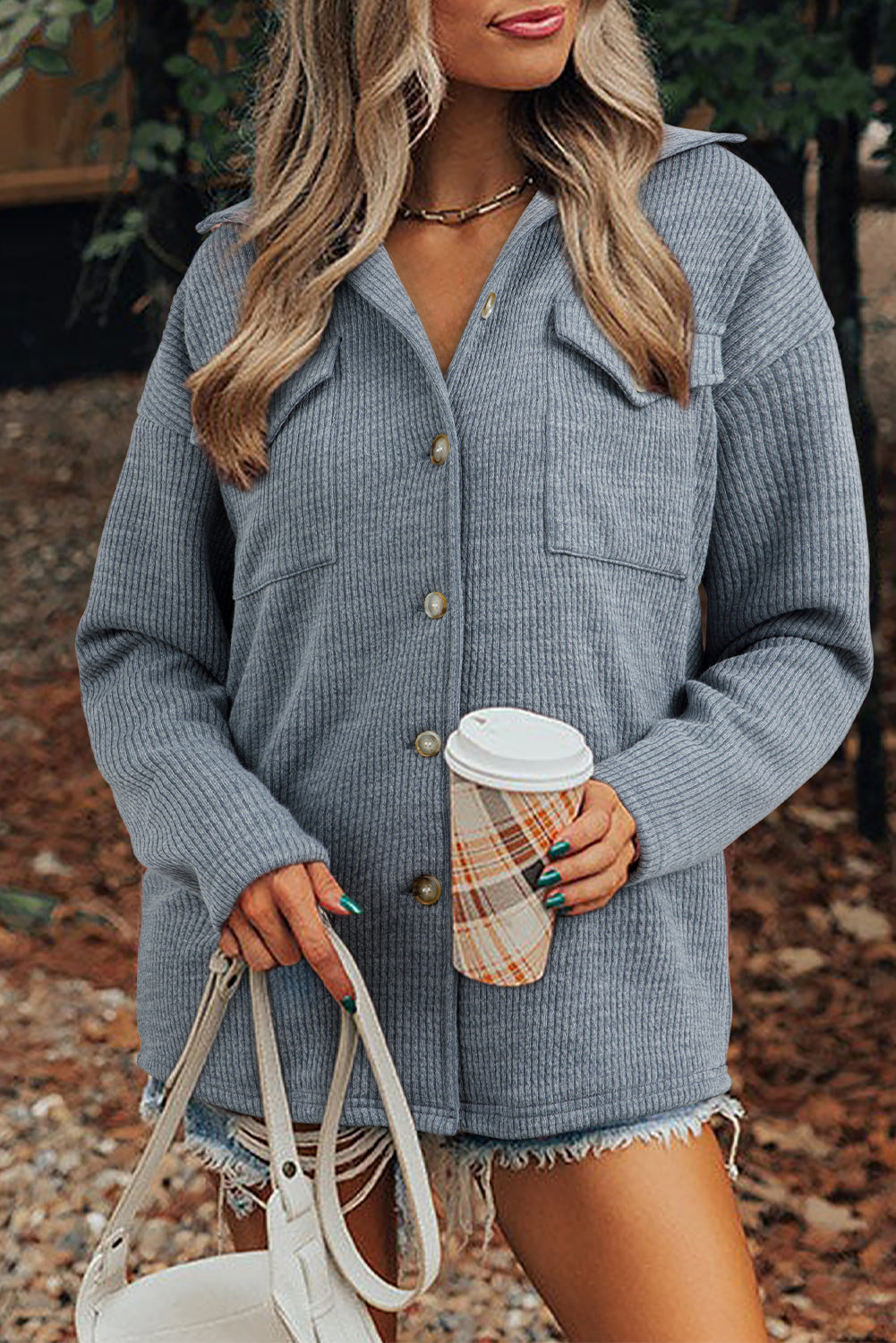Woman wearing a gray textured jacket holding a coffee cup outdoors.
