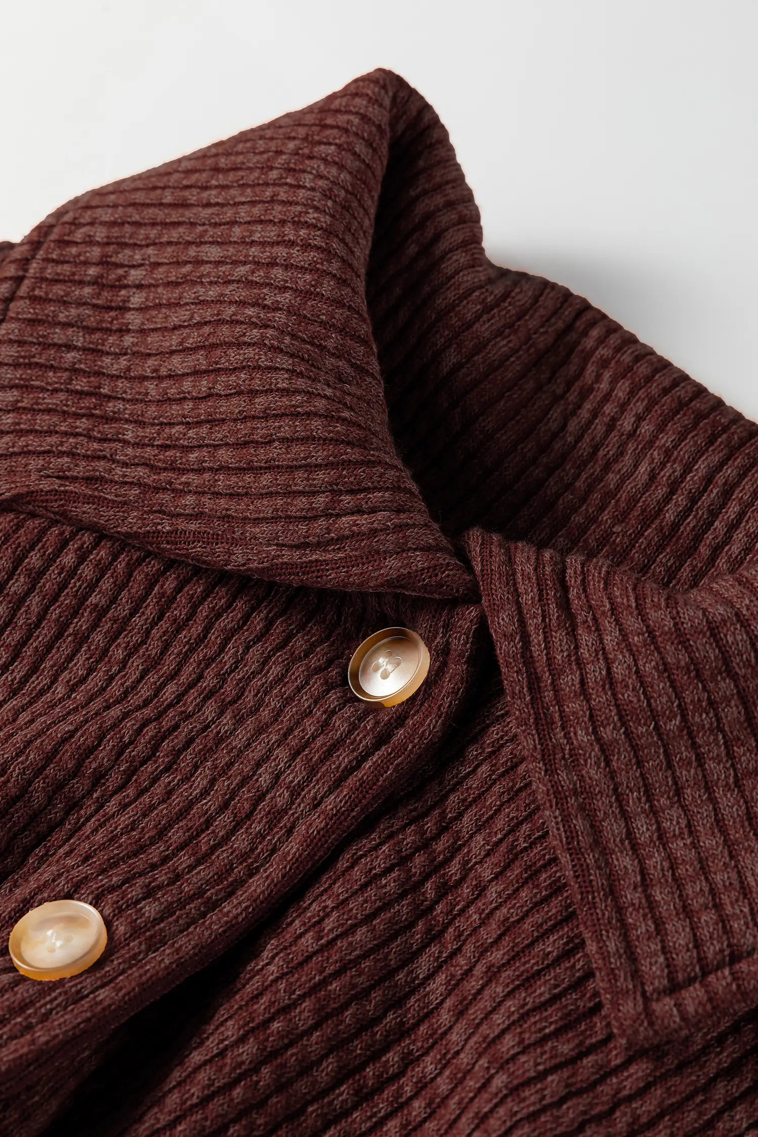 Close-up of a brown ribbed sweater with buttons on a light background
