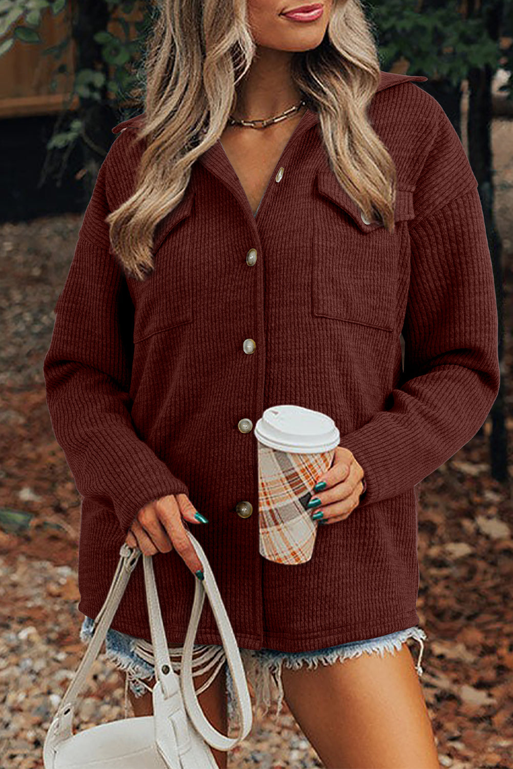 Woman wearing a brown cardigan holding a coffee cup and white handbag outdoors.