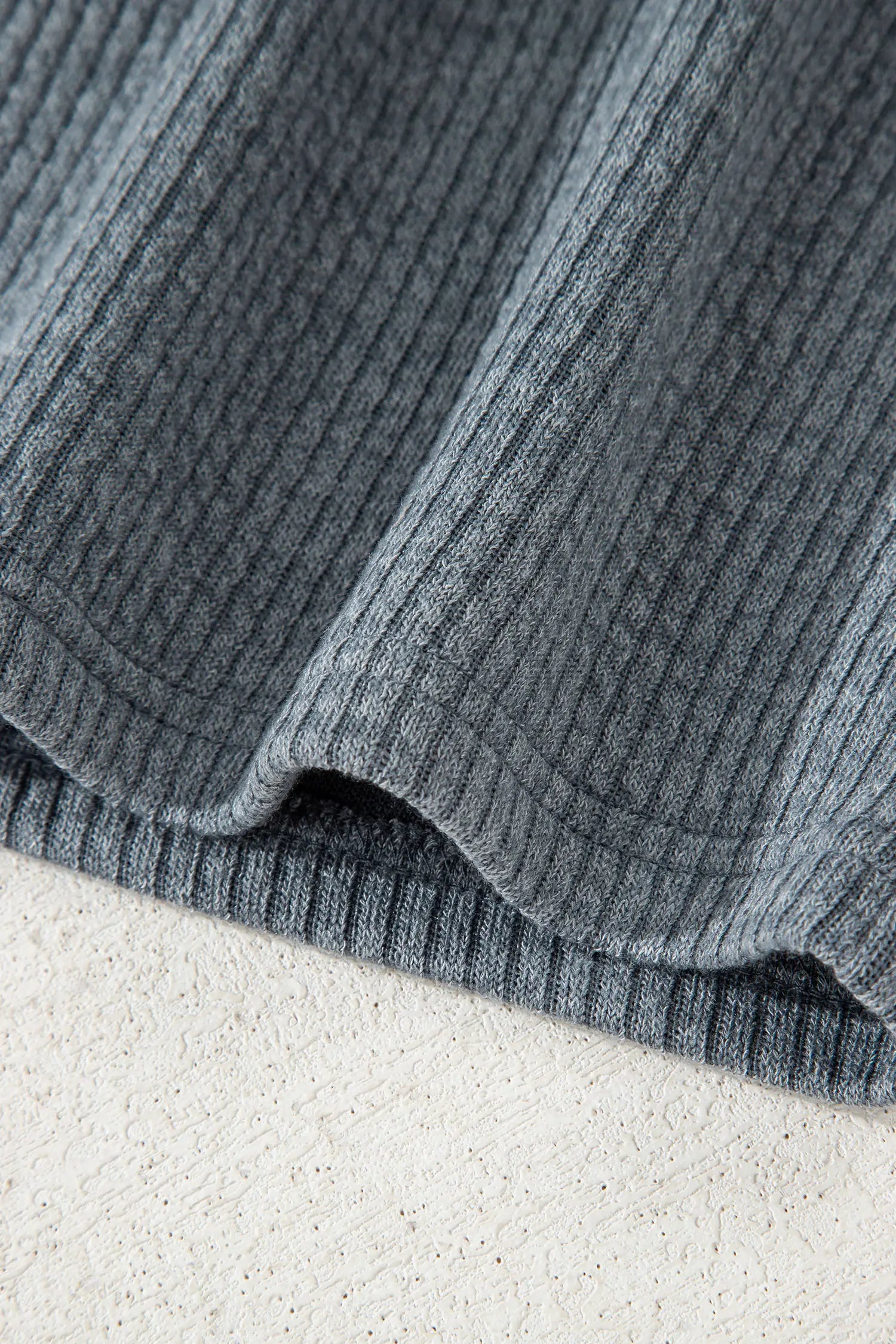 Close-up of a ribbed knit fabric in a muted blue-gray color, draped over a light textured surface.