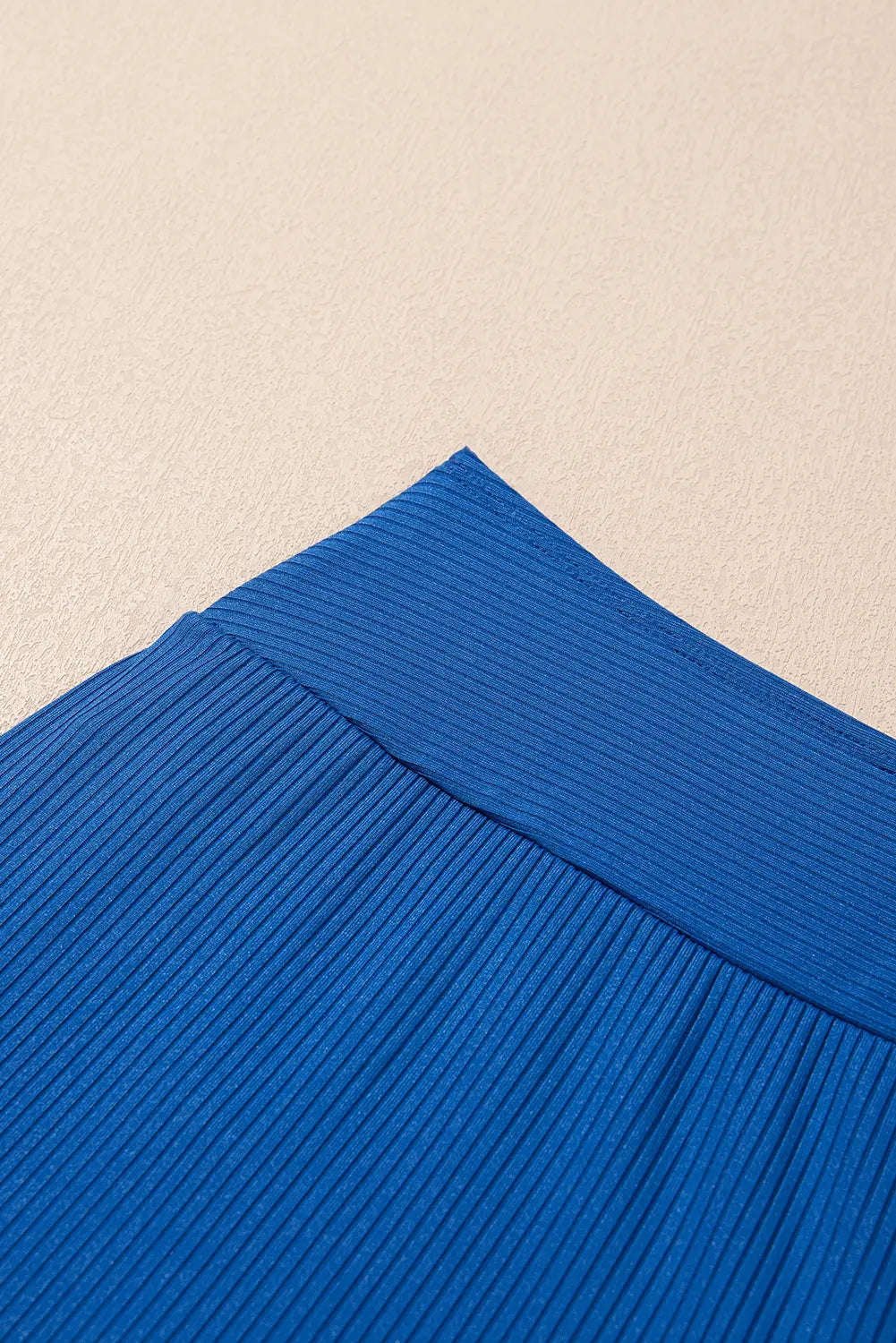 Close-up of a bright blue ribbed fabric corner against a light beige textured background.