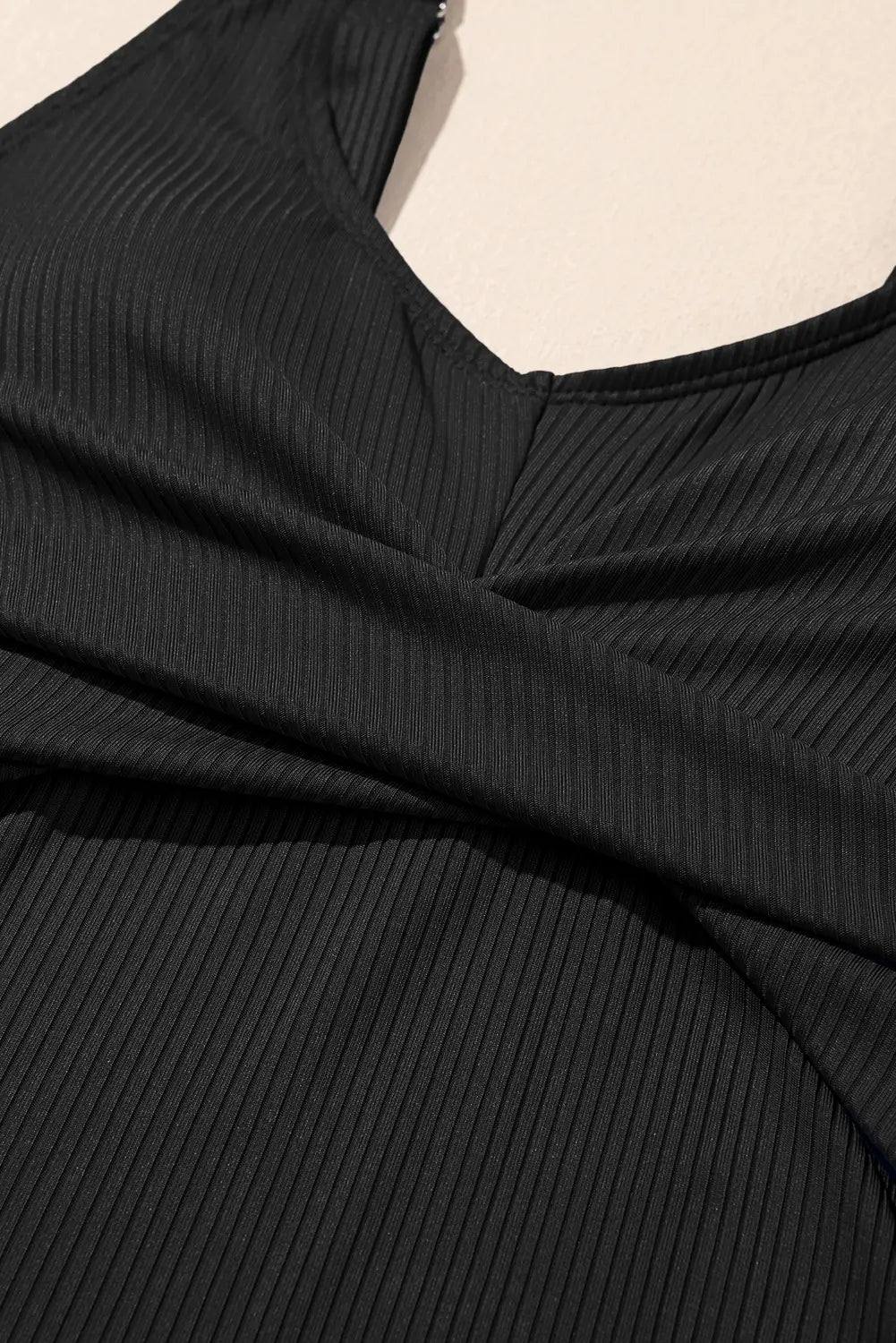 Close-up of a black ribbed garment with a V-neckline on a beige background