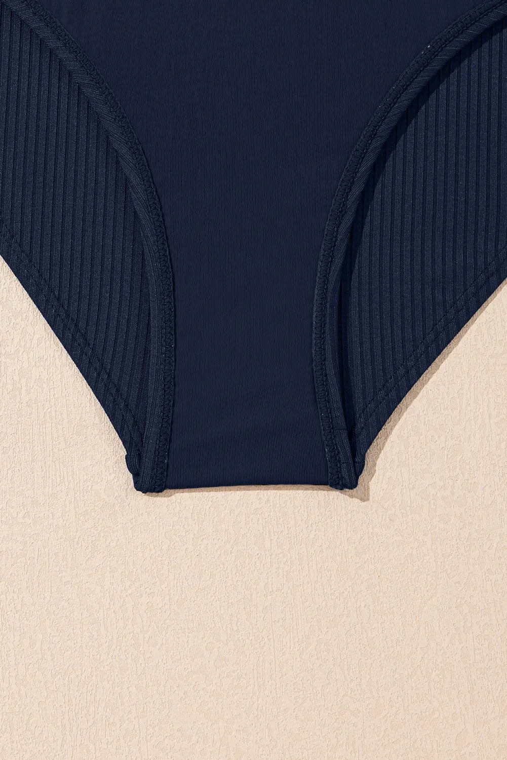Navy blue ribbed swimsuit bottom on a beige background