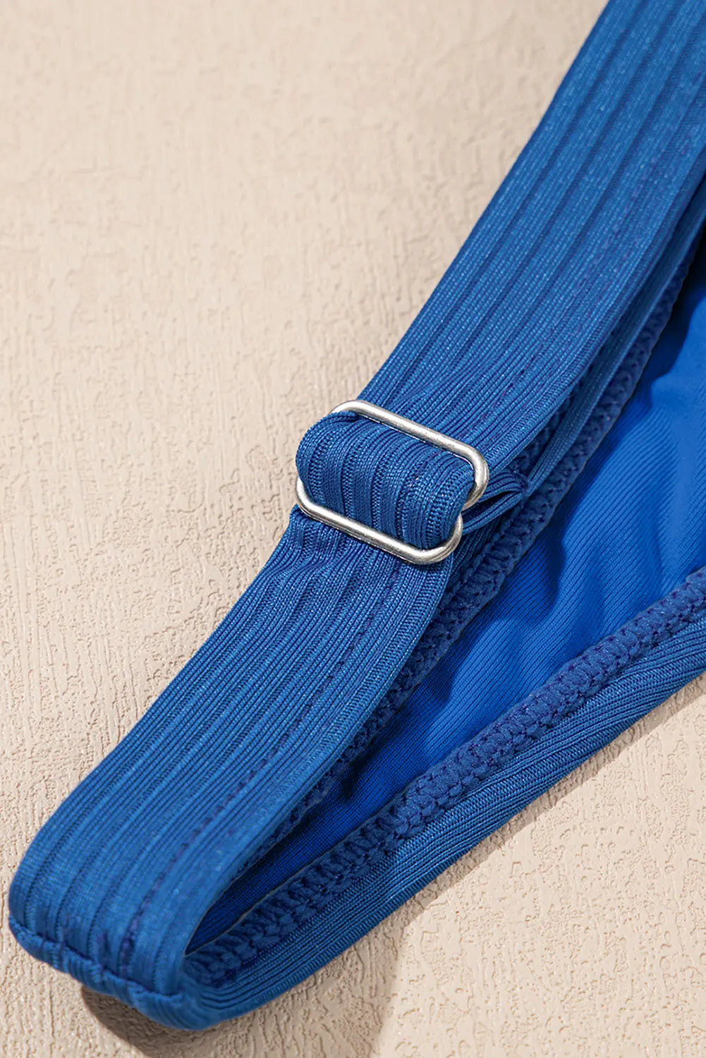 Blue yoga strap with a metal buckle on a beige surface