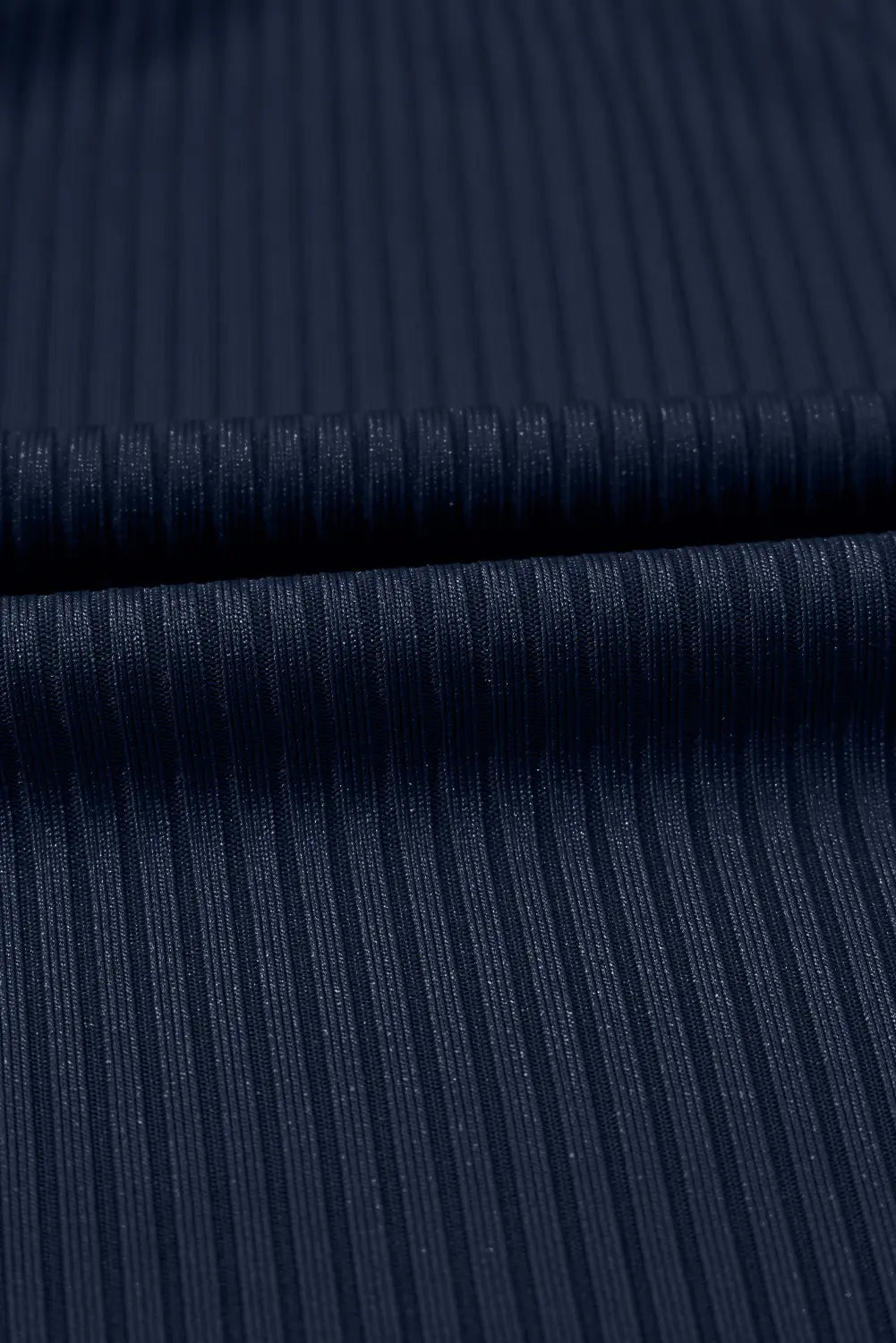 Close-up of dark navy ribbed fabric with a fine vertical stripe texture and a horizontal fold.