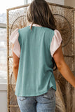 Person wearing a teal ribbed tank top and light pink sleeves, standing in front of a textured wall.