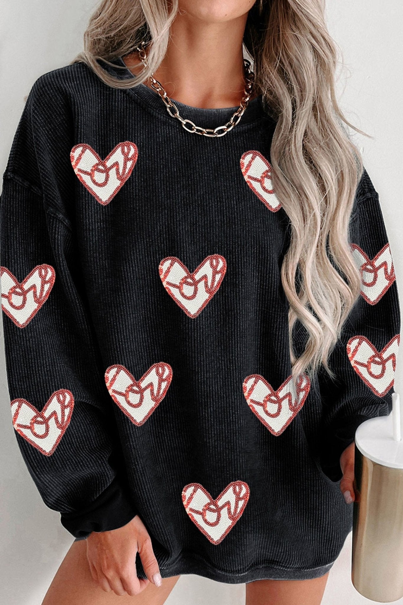 Black sweater with red heart patterns worn by a person with long blonde hair.