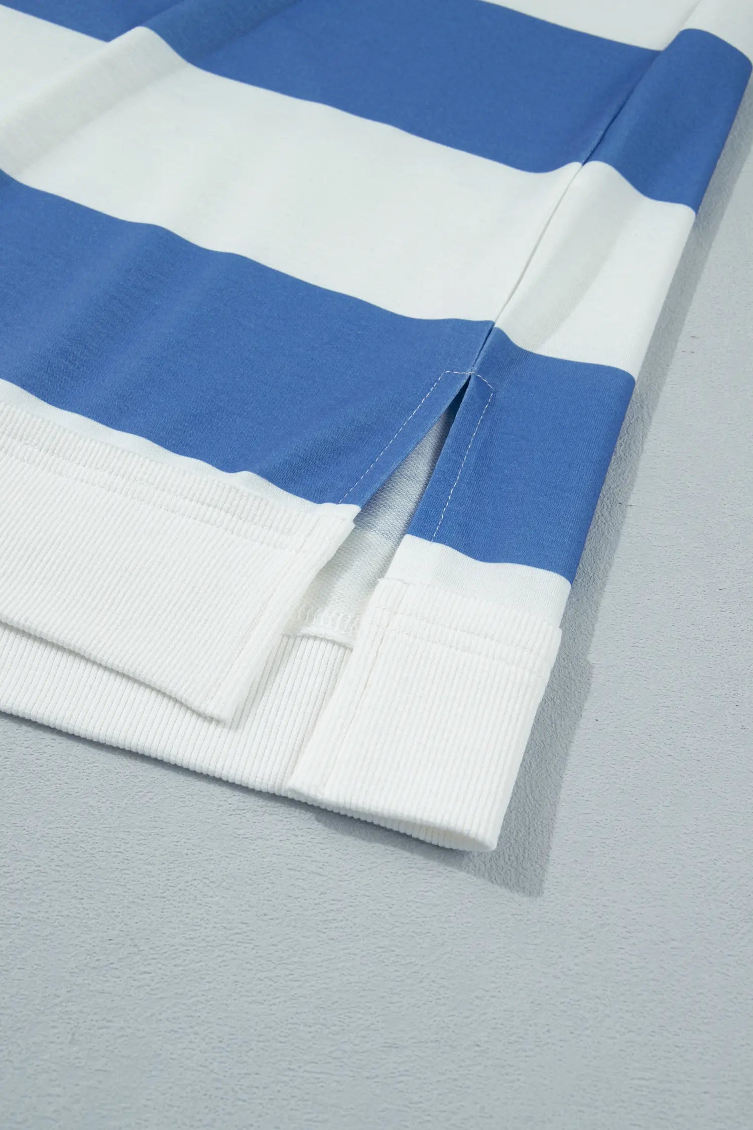 A close-up of a blue and white horizontally striped knit garment, showing the ribbed cuff and folded fabric on a light gray surface.