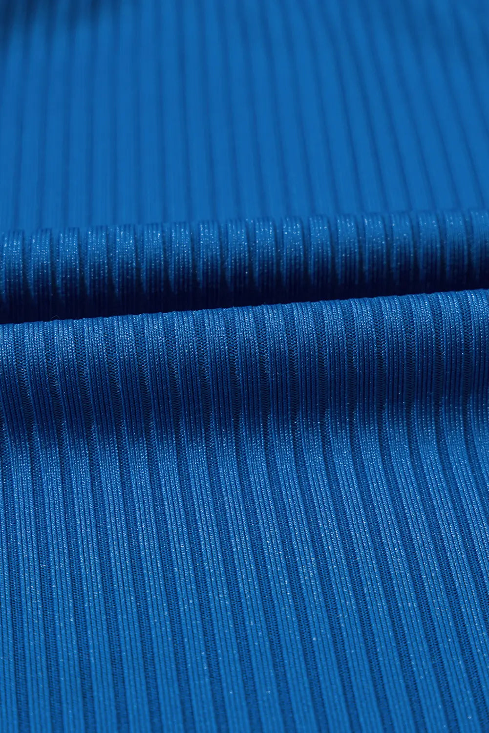 A close-up of bright blue ribbed fabric with a fine vertical texture and a horizontal fold running across the center.
