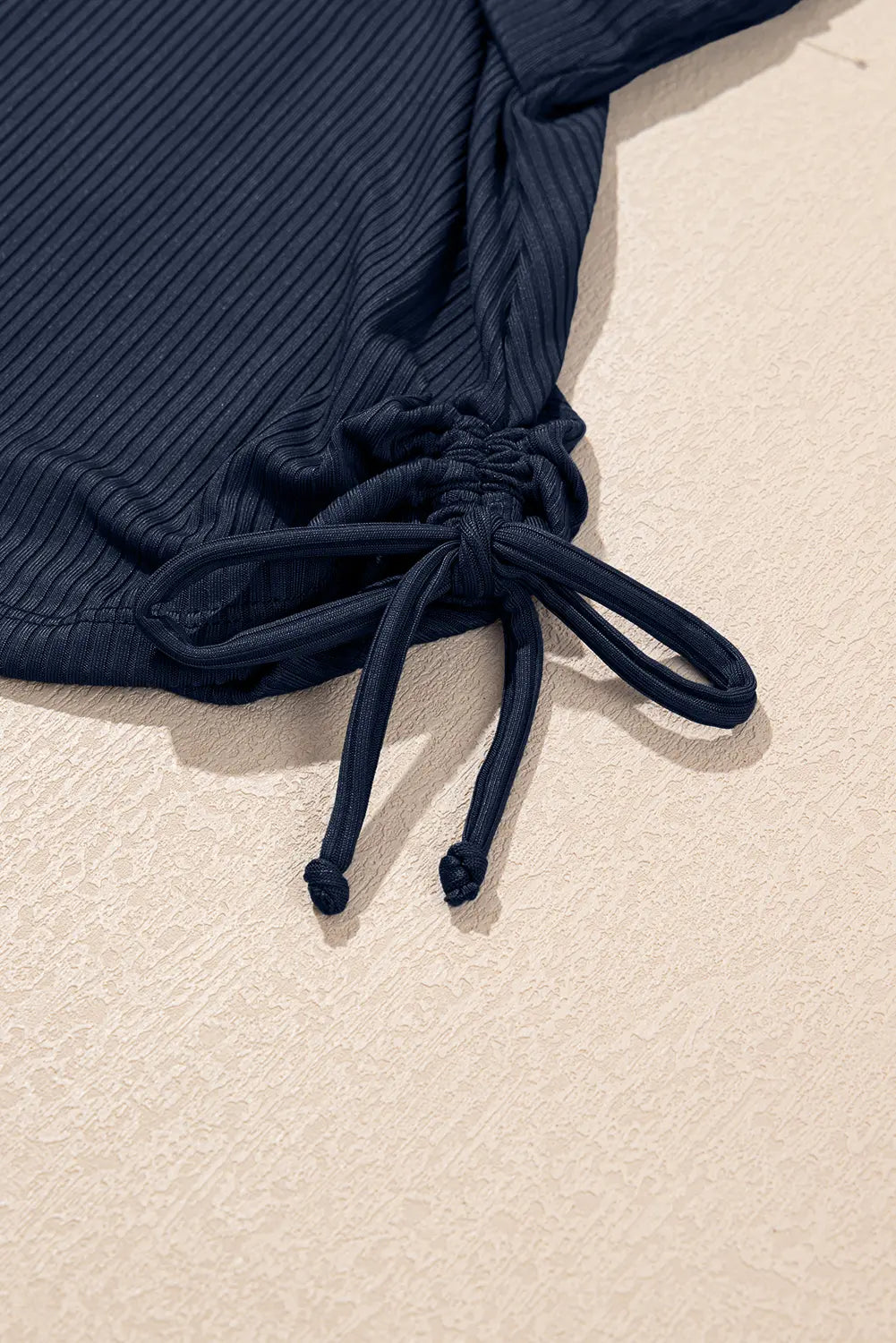 Navy blue ribbed swimsuit top with tie detail on a beige background