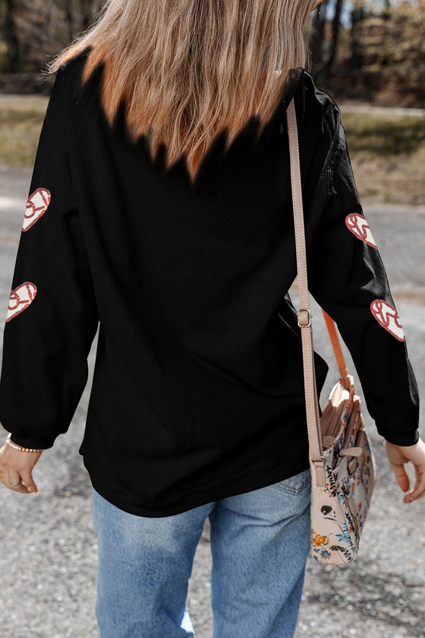 Person wearing a black jacket with red patterns, holding a floral bag outdoors.