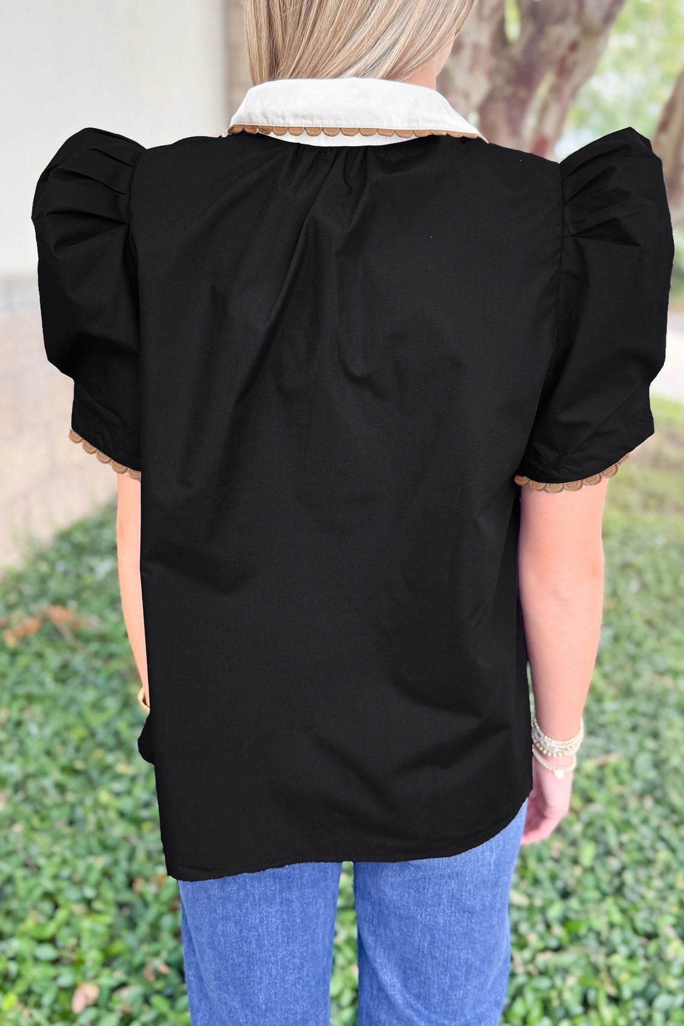 Person wearing a black top with ruffled sleeves and a white collar, standing outdoors.