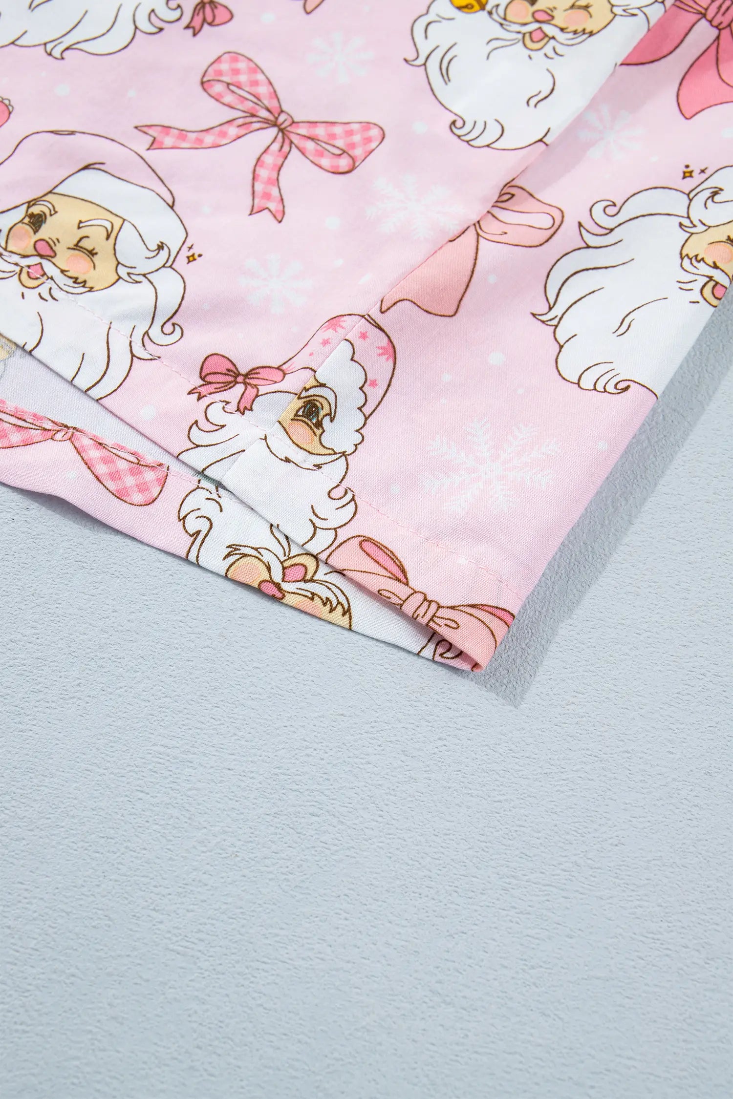 Close-up of light pink fabric with cartoon Santa print and gold details.