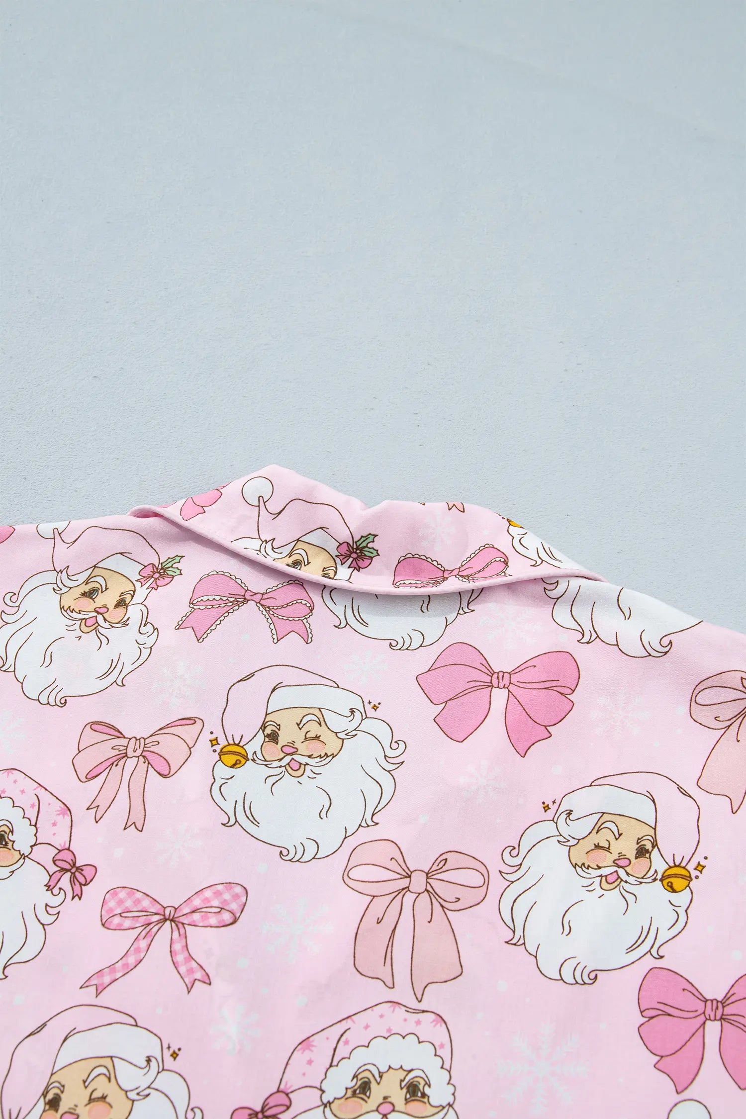 Close-up of pink fabric with cartoon Santa faces and pink bow print.