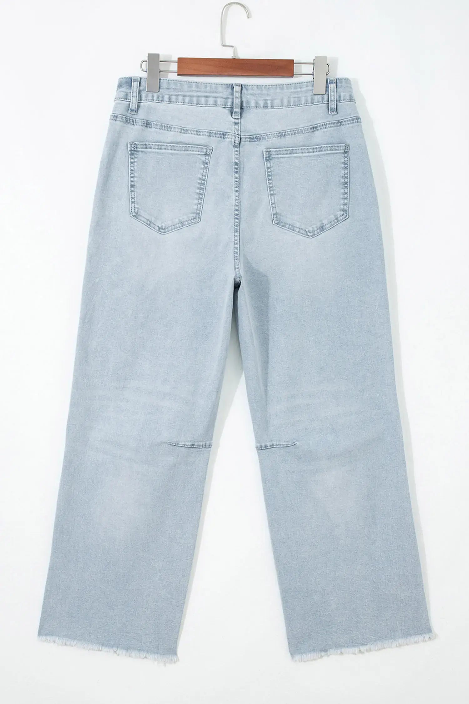 Light wash blue denim jeans shown from the back, hanging on a wooden hanger against a plain white background.