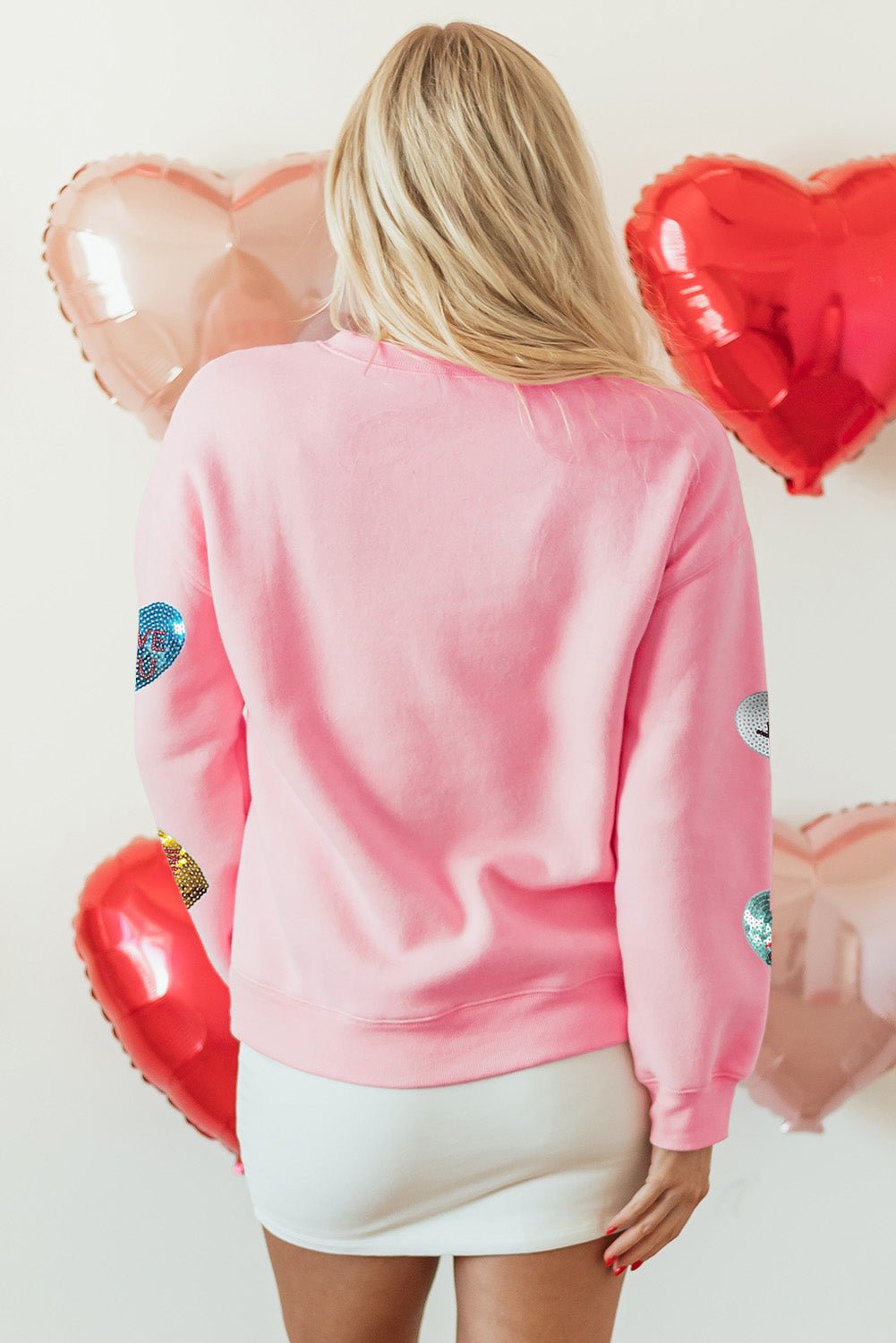 Person wearing a pink sweatshirt with heart designs in front of heart-shaped balloons.