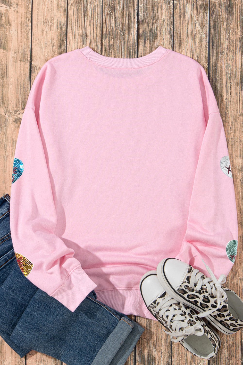 Pink long-sleeve shirt with colorful sleeves on a wooden surface, paired with jeans and leopard print sneakers.