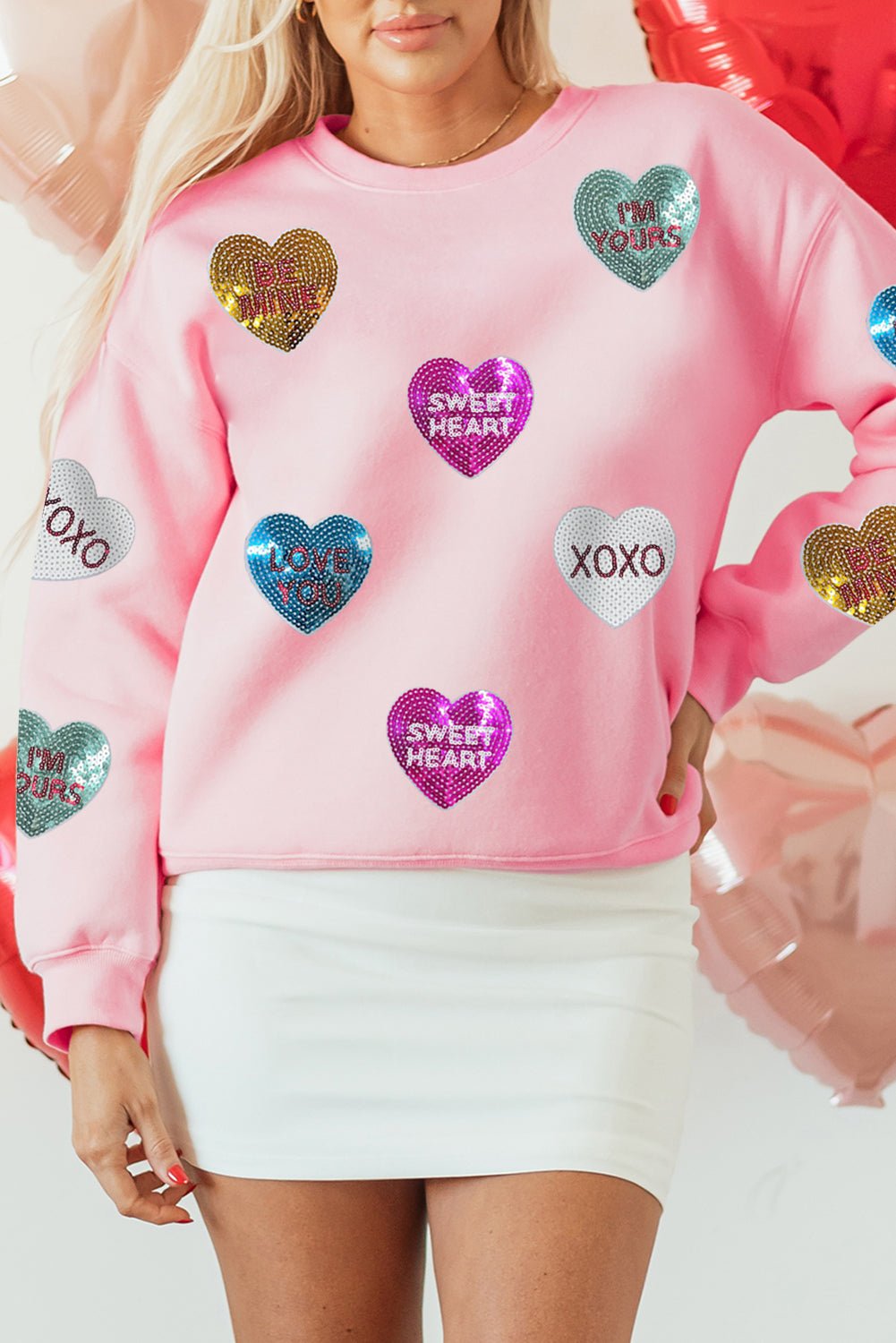 Person wearing a pink sweatshirt with colorful heart-shaped sequins on a white background