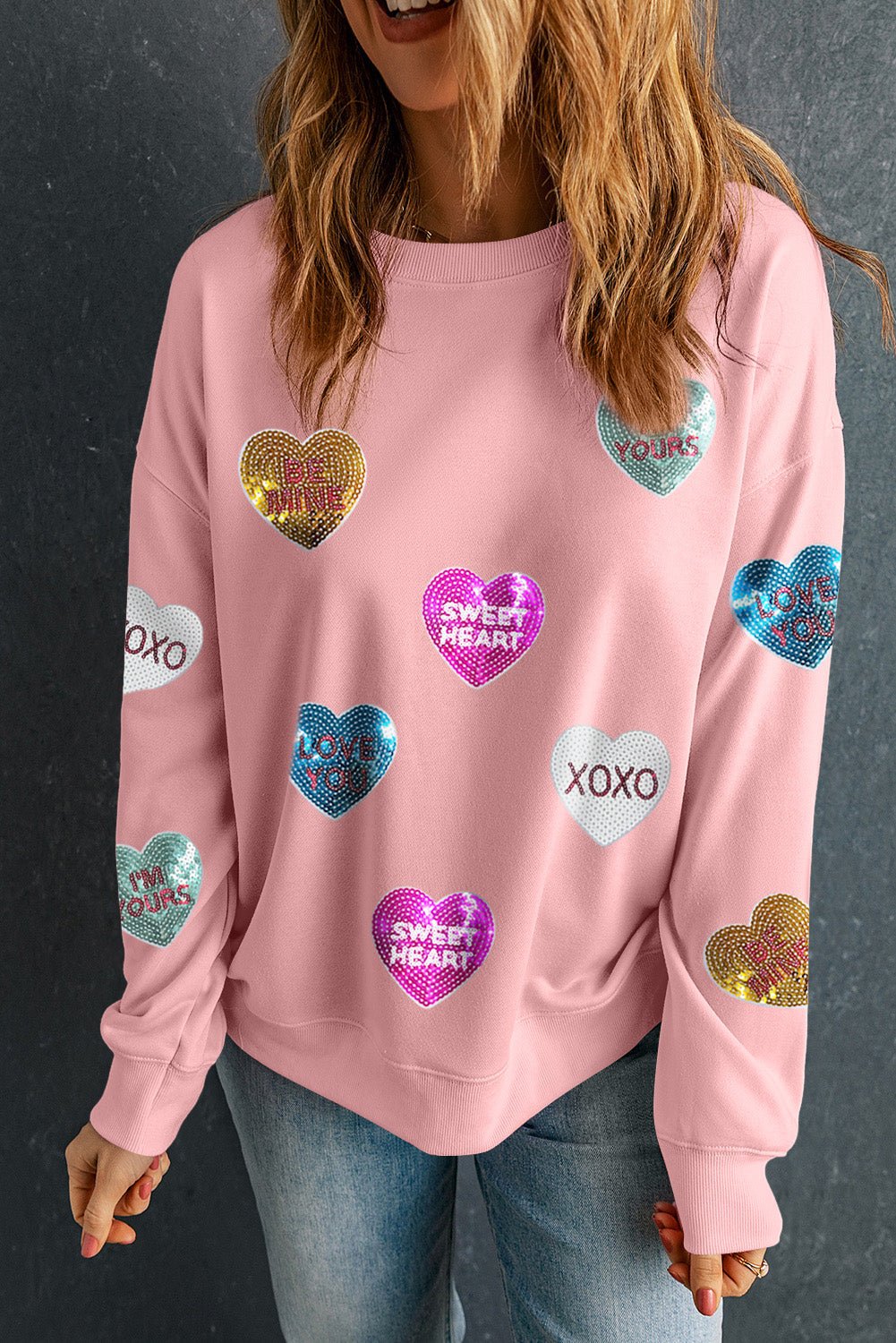 Person wearing a pink sweatshirt with heart-shaped sequin designs on a dark background