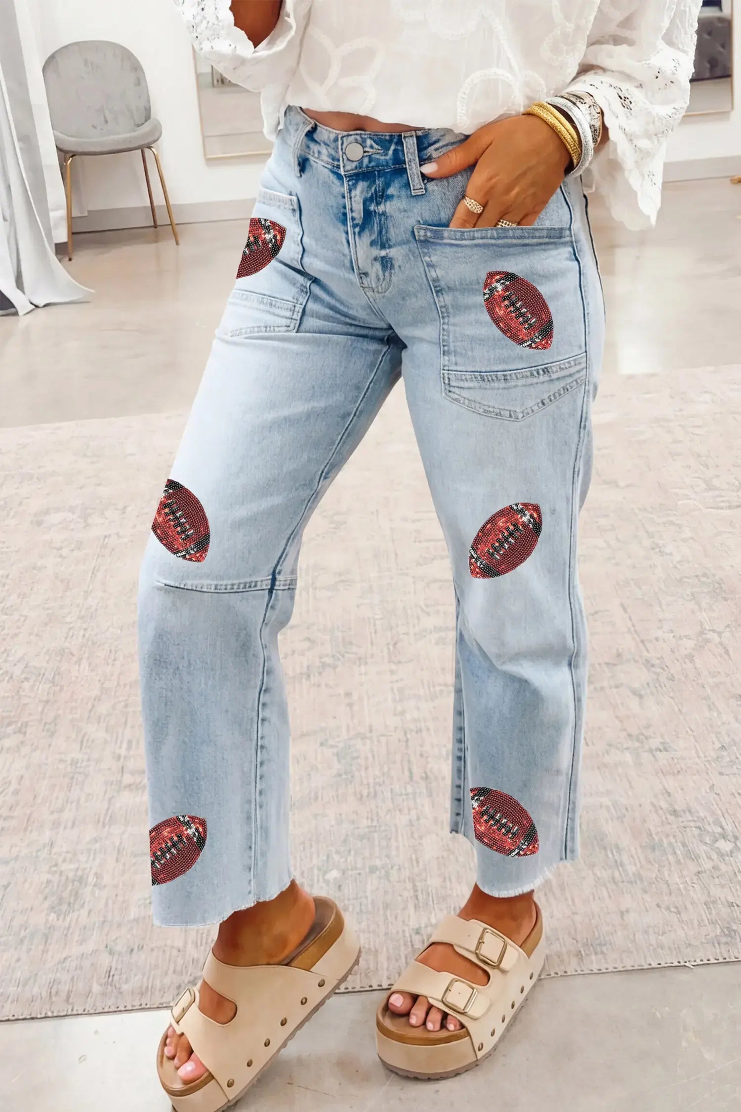 Light wash blue denim jeans with embroidered football patches on the thighs and lower legs, worn by a model in a bright indoor setting.