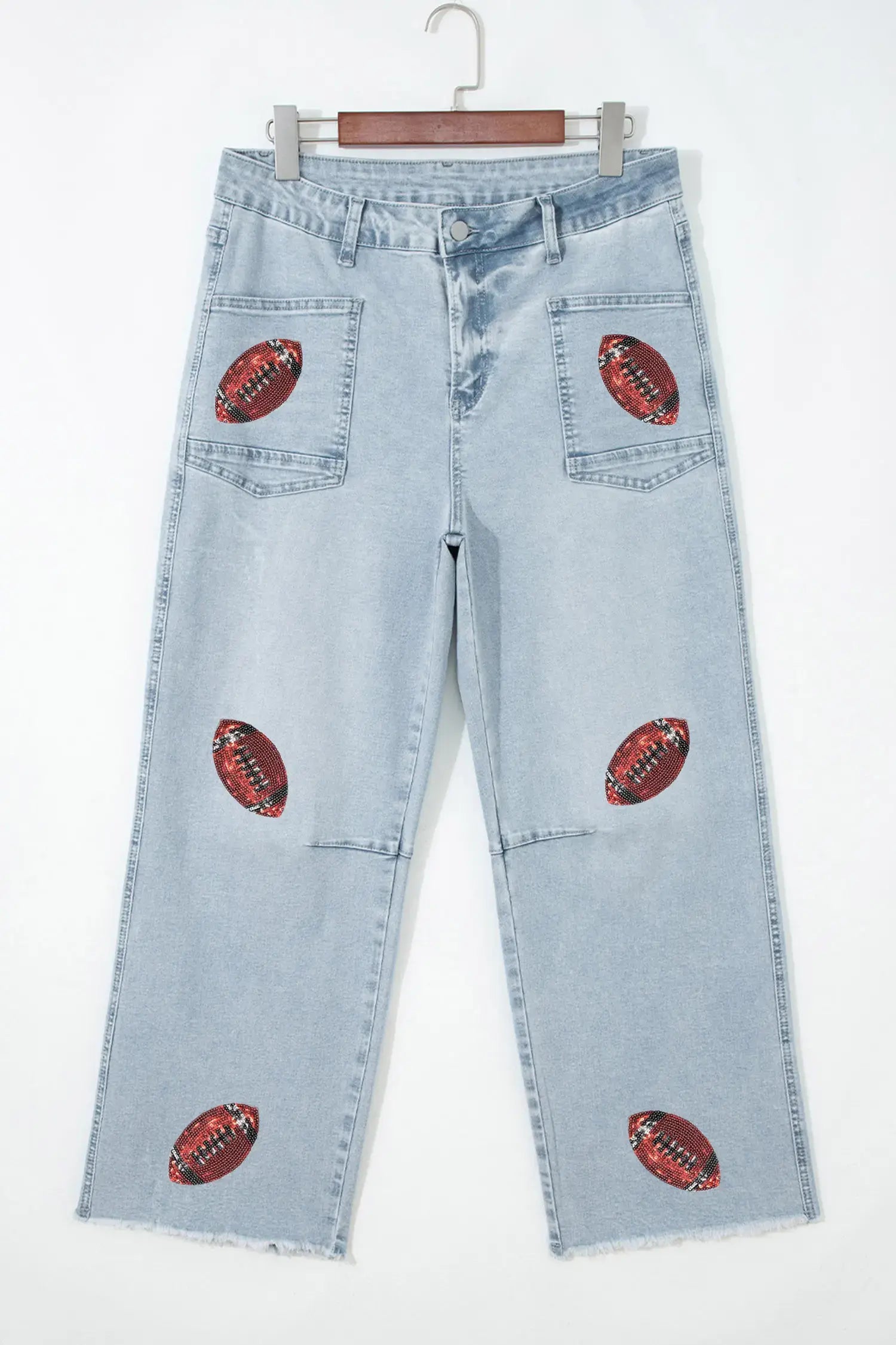 Light wash blue denim jeans with embroidered red and brown football patches on the back pockets and scattered down the front legs, hanging on a wooden hanger against a white background.