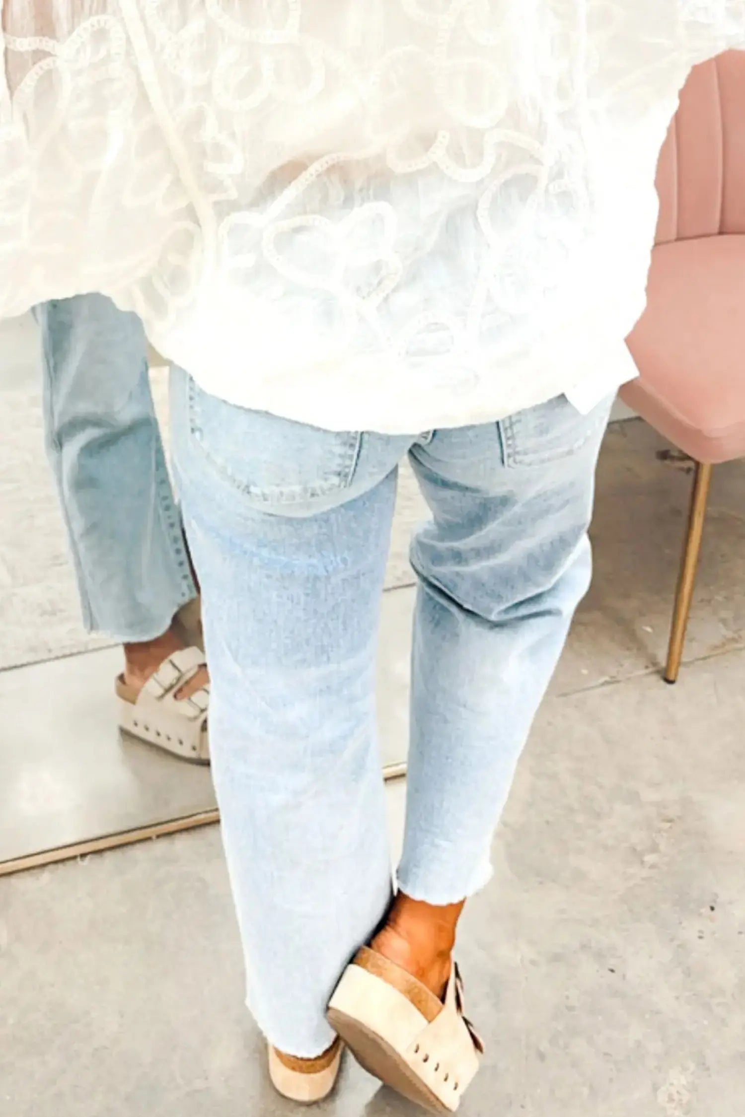 A person wearing light-wash blue jeans, a white lace-trim top, and beige platform sandals, shown from the back in an indoor setting.