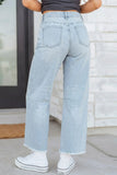 A person shown from the back wearing light-wash wide-leg cropped jeans, a dark gray crop top, and white sneakers in front of a white brick wall.