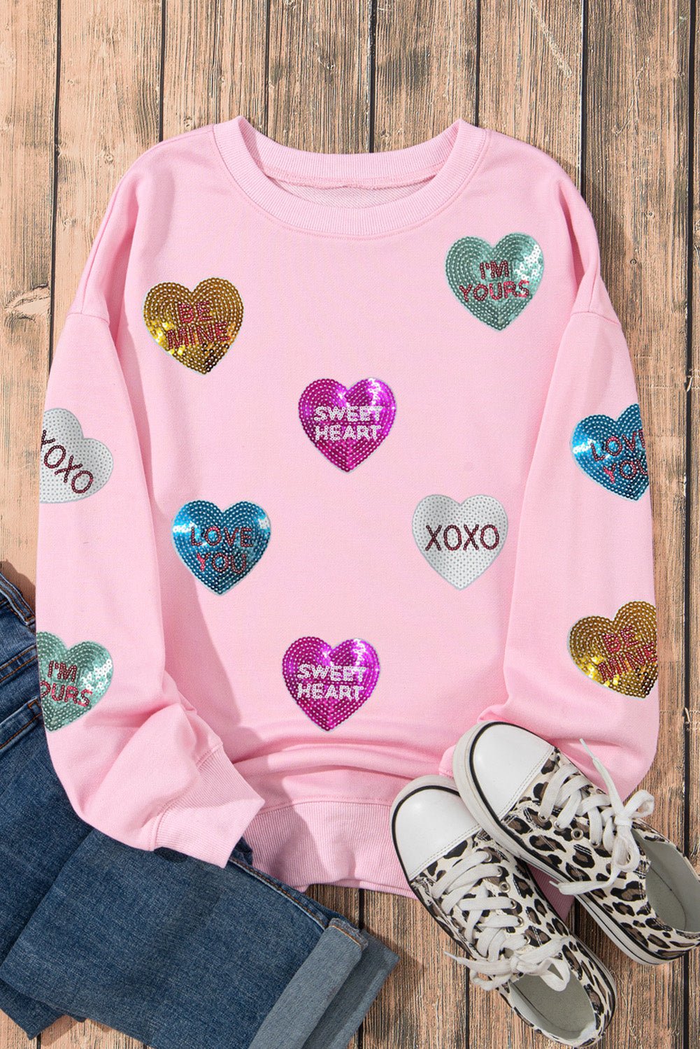 Pink sweatshirt with heart-shaped sequin designs on a wooden surface