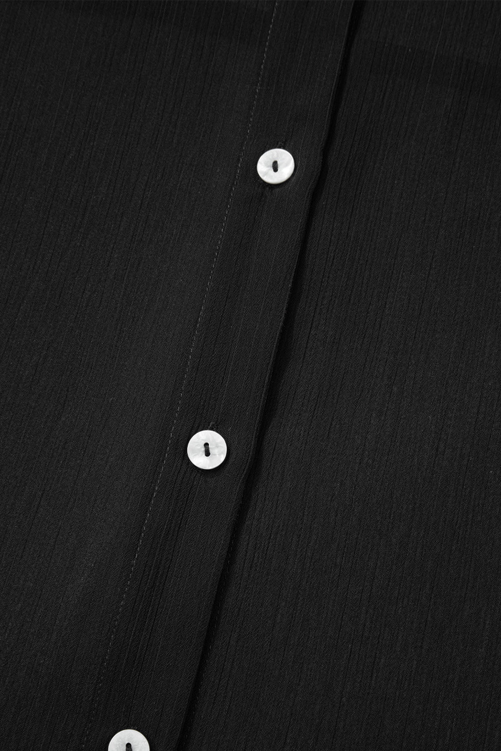 Close-up of a black shirt with white buttons on a black background