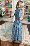 Woman in a blue patterned dress standing in a store with colorful products on shelves.