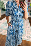 A woman takes a mirror selfie in a boutique wearing a blue and white geometric patterned midi dress with short sleeves, a collared neckline, and a smocked waist.