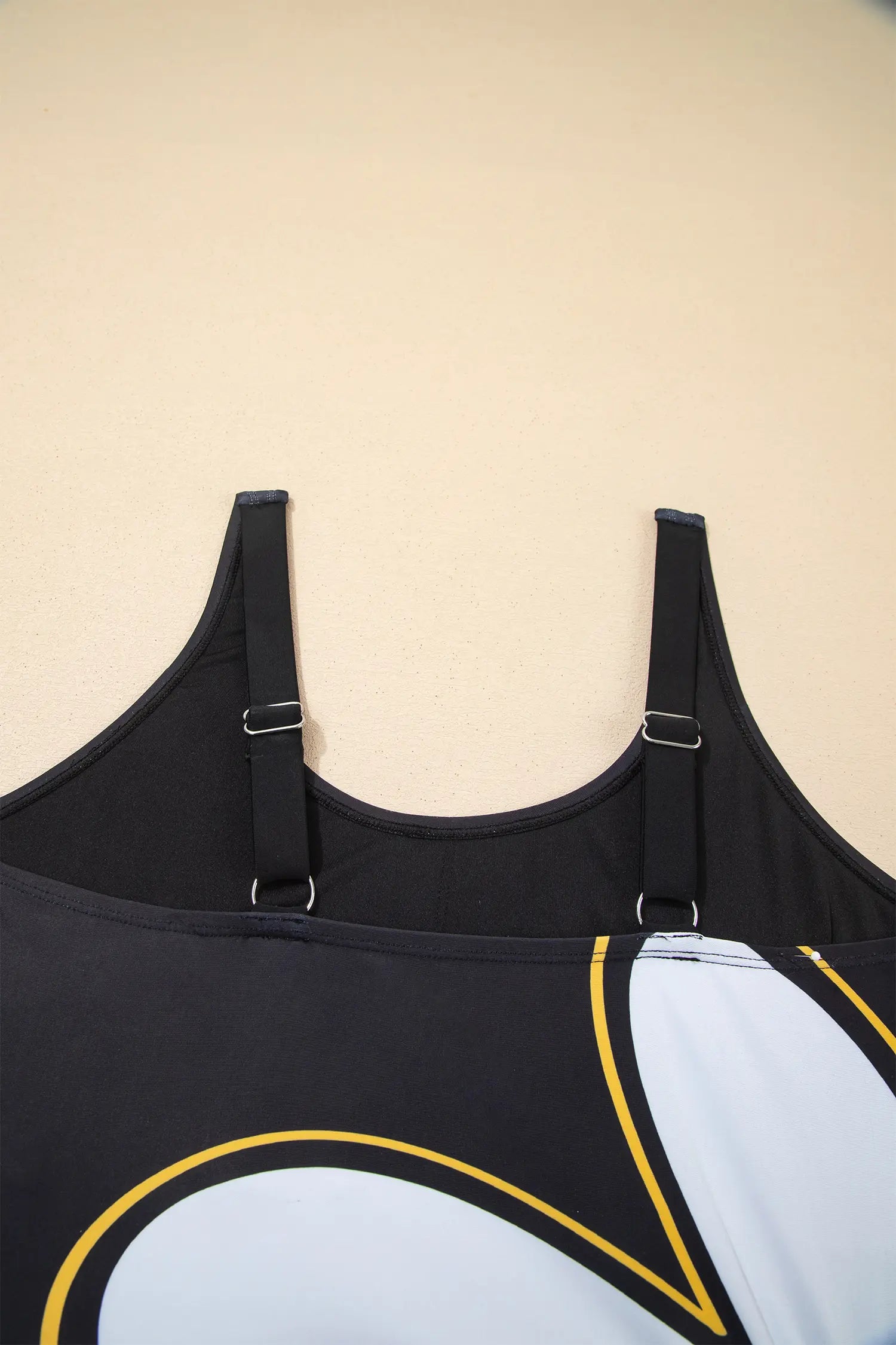 Close-up of the back straps and upper back of a black athletic tank top with adjustable straps, shown against a plain beige background.