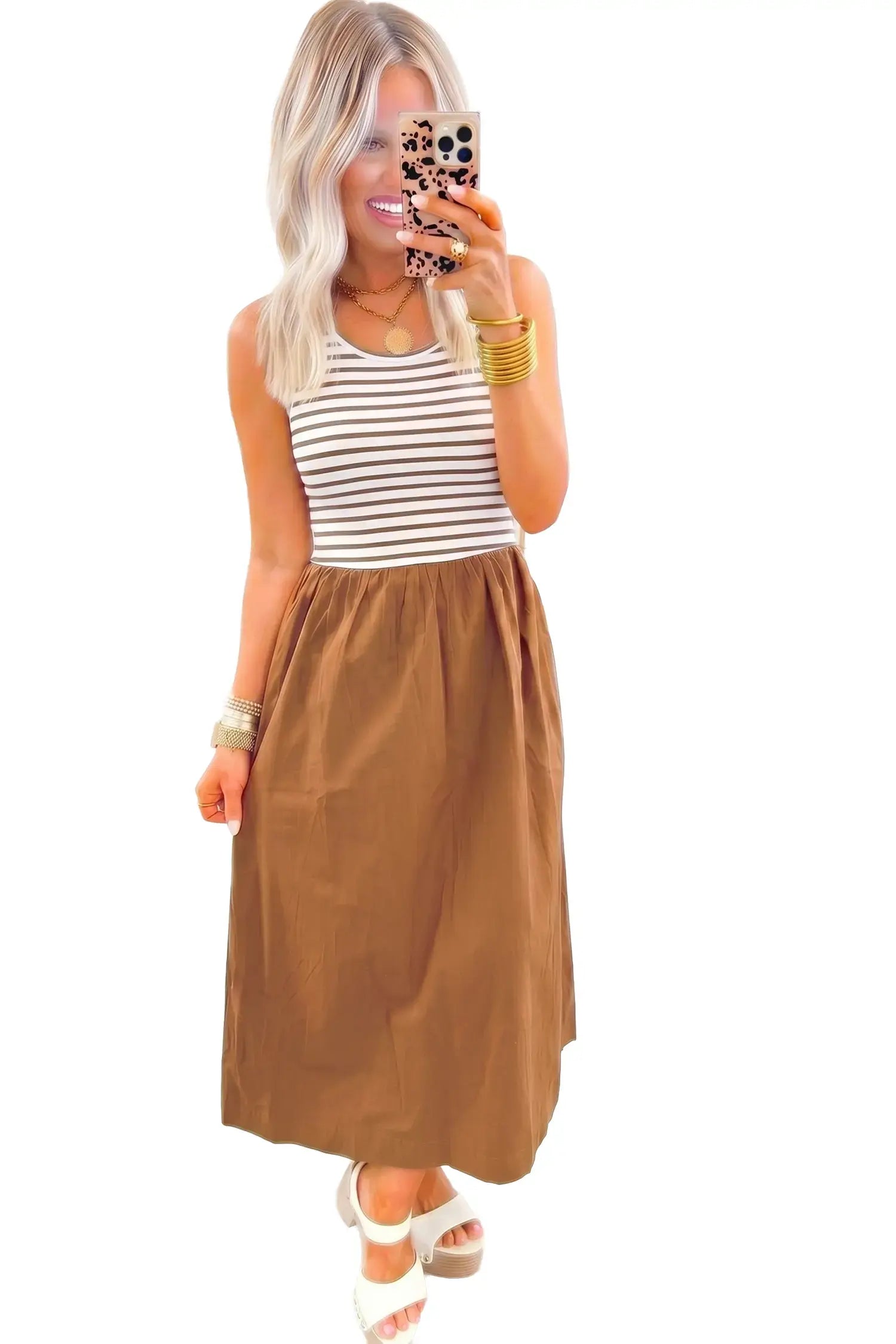Woman taking a mirror selfie wearing a striped tank top and brown skirt on a white background