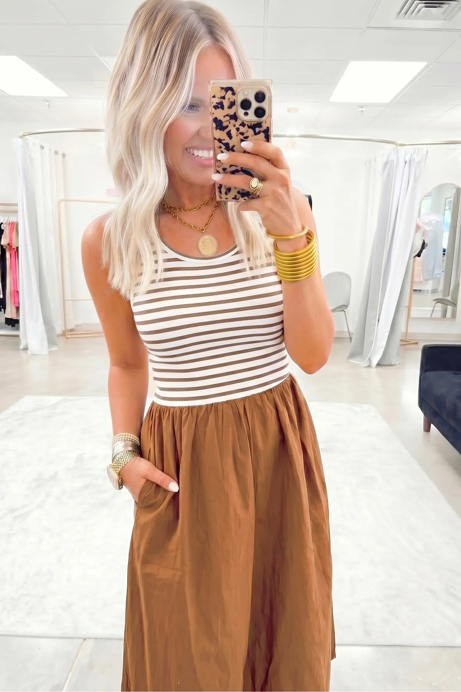 Woman taking a mirror selfie wearing a striped tank top and brown pants in a store.