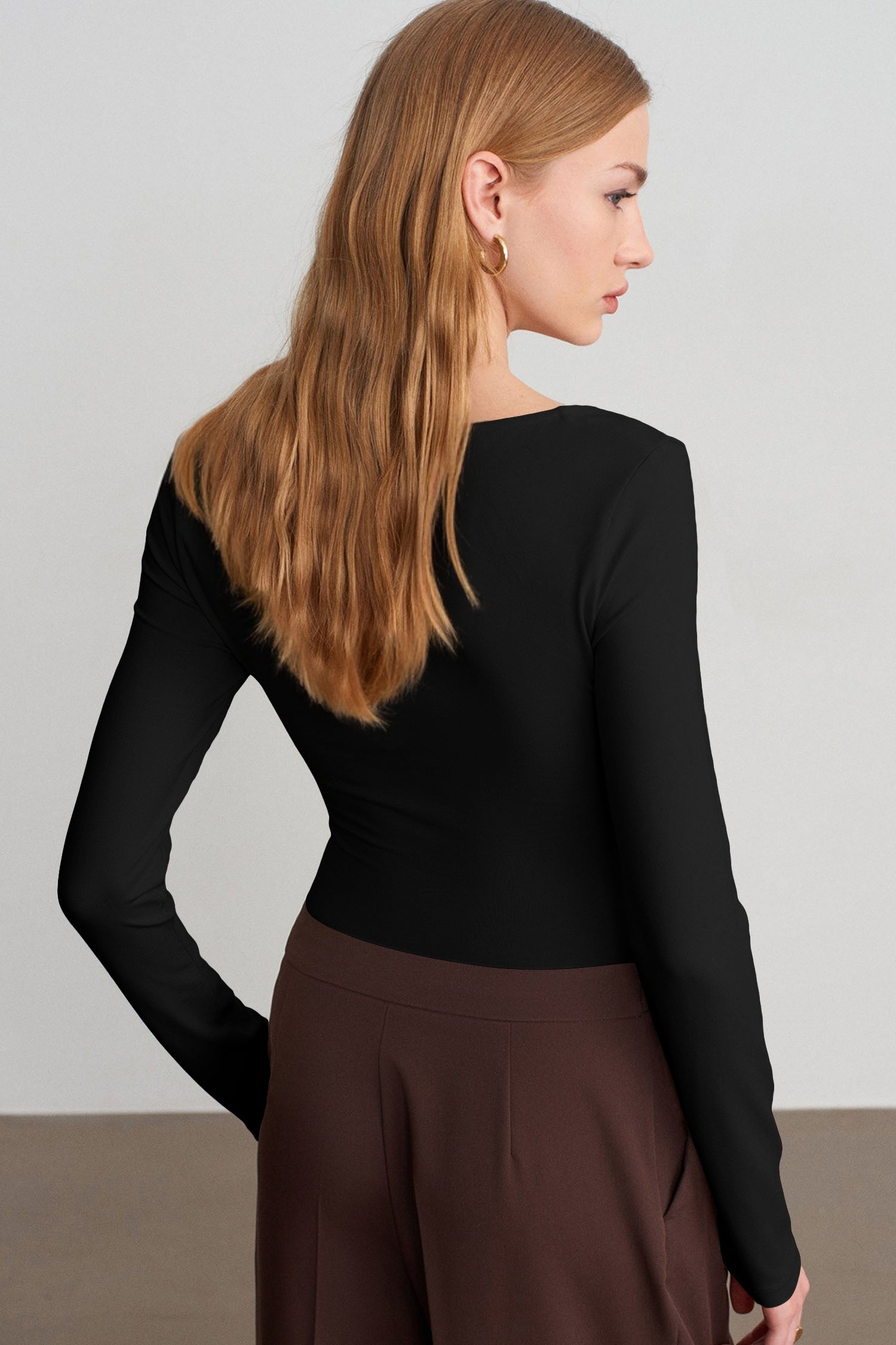 Back view of woman in fitted black top with brown trousers.
