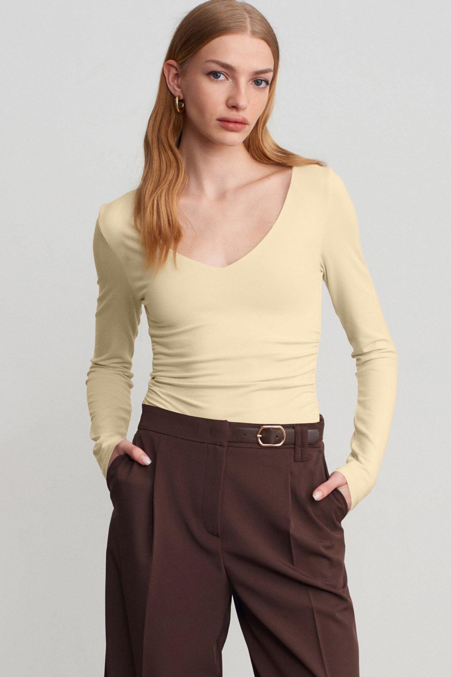 Woman in fitted light cream V-neck top with dark brown trousers.