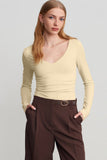Woman in fitted light cream V-neck top with dark brown trousers.