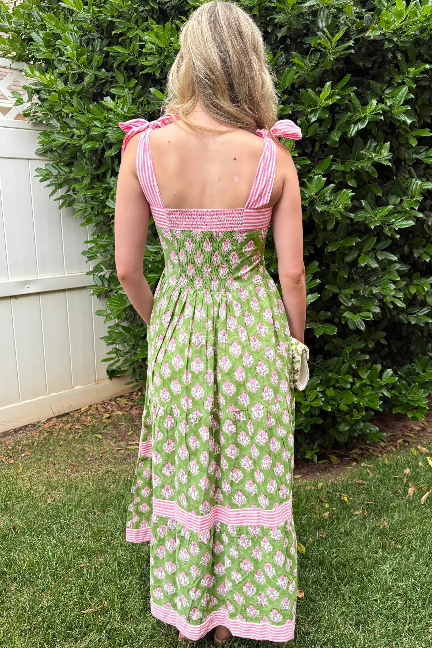 Woman wearing a green and pink dress with floral pattern standing in front of a bush.