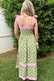 Woman wearing a green and pink dress with floral pattern standing in front of a bush.