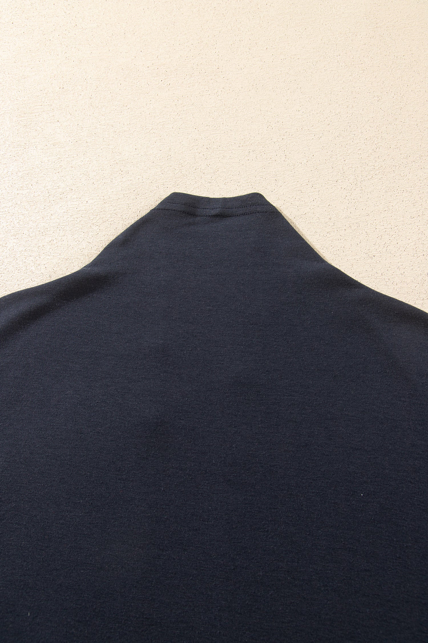 A close-up of a dark navy blue knit fabric, likely a turtleneck sweater or top, laid flat 