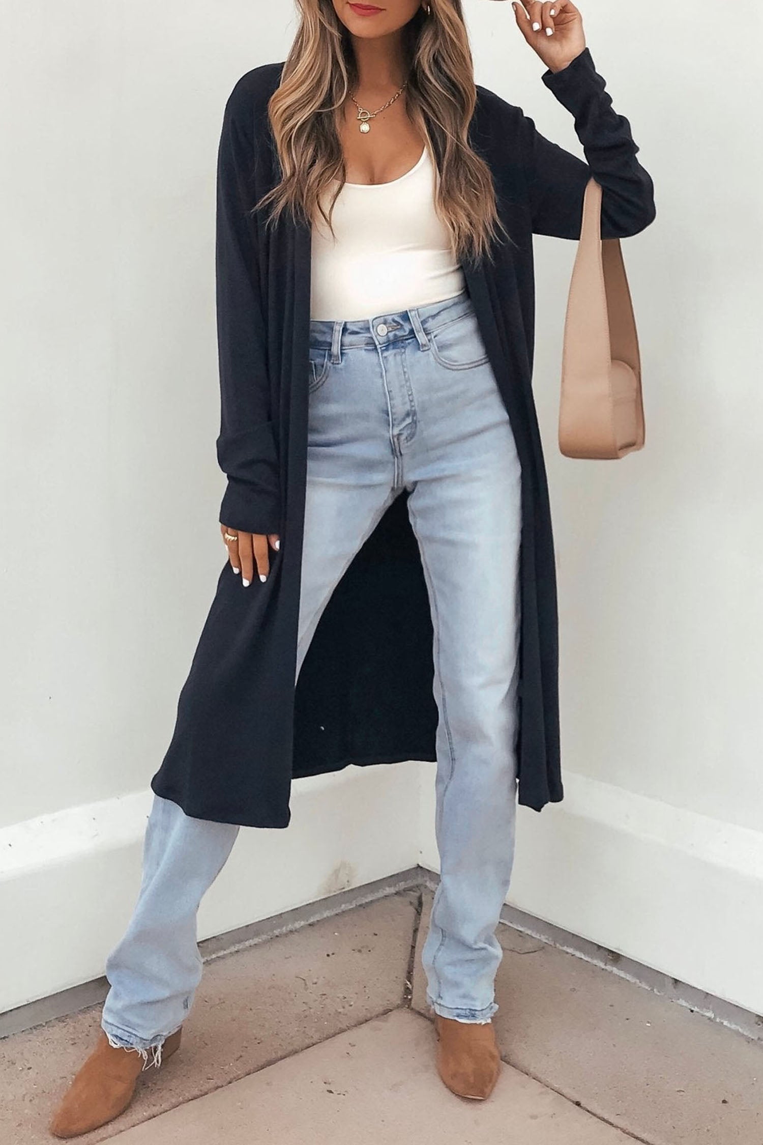Woman in long black open-front cardigan, white tank, blue jeans, and beige tote.
