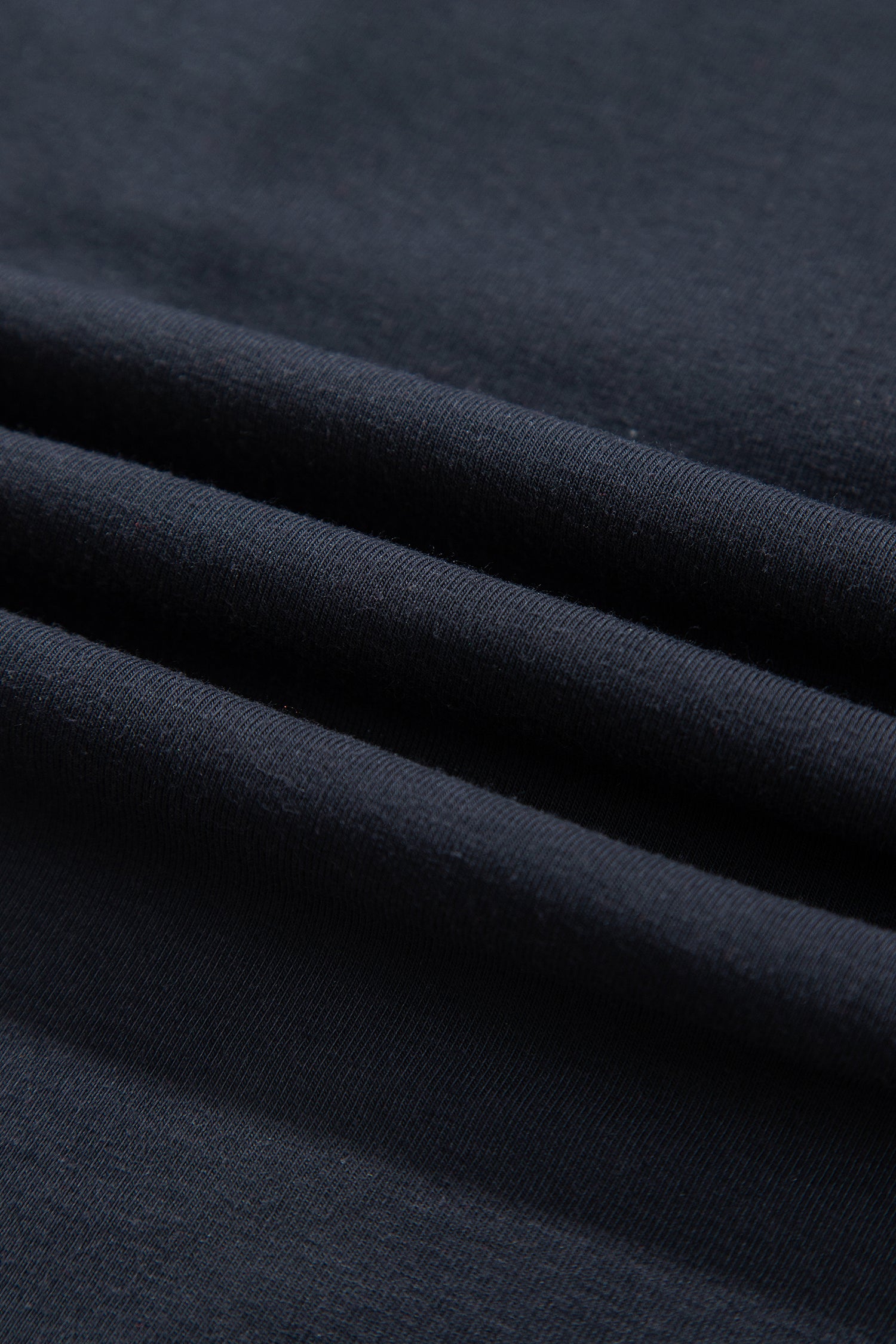 A close-up of dark navy blue fabric with soft diagonal folds showing the texture and weave.