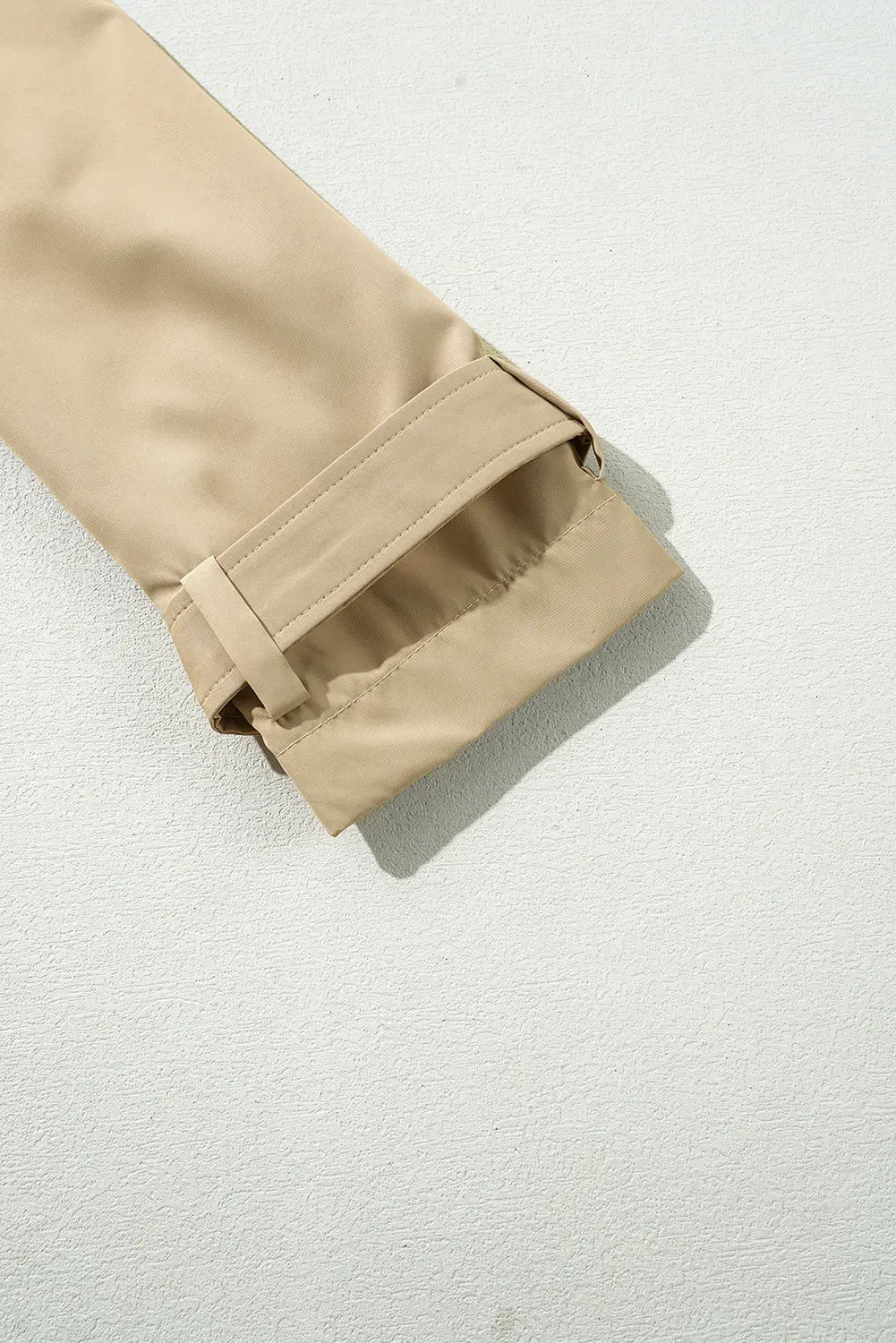 A close-up of a beige trench coat sleeve with a turned-up cuff.