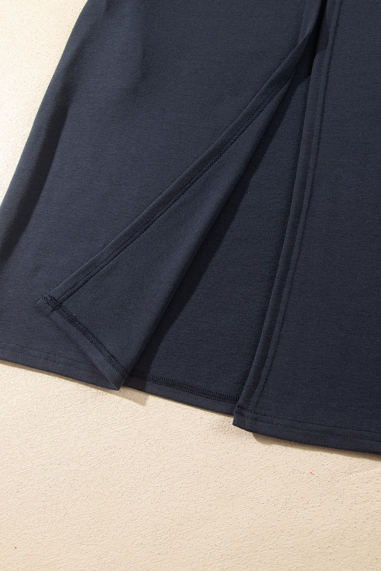 Close-up of a dark navy blue garment laid flat on a light beige surface, showing folded fabric and stitched edges.