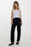 Woman wearing a white sleeveless top and black pants with a star design on a white background