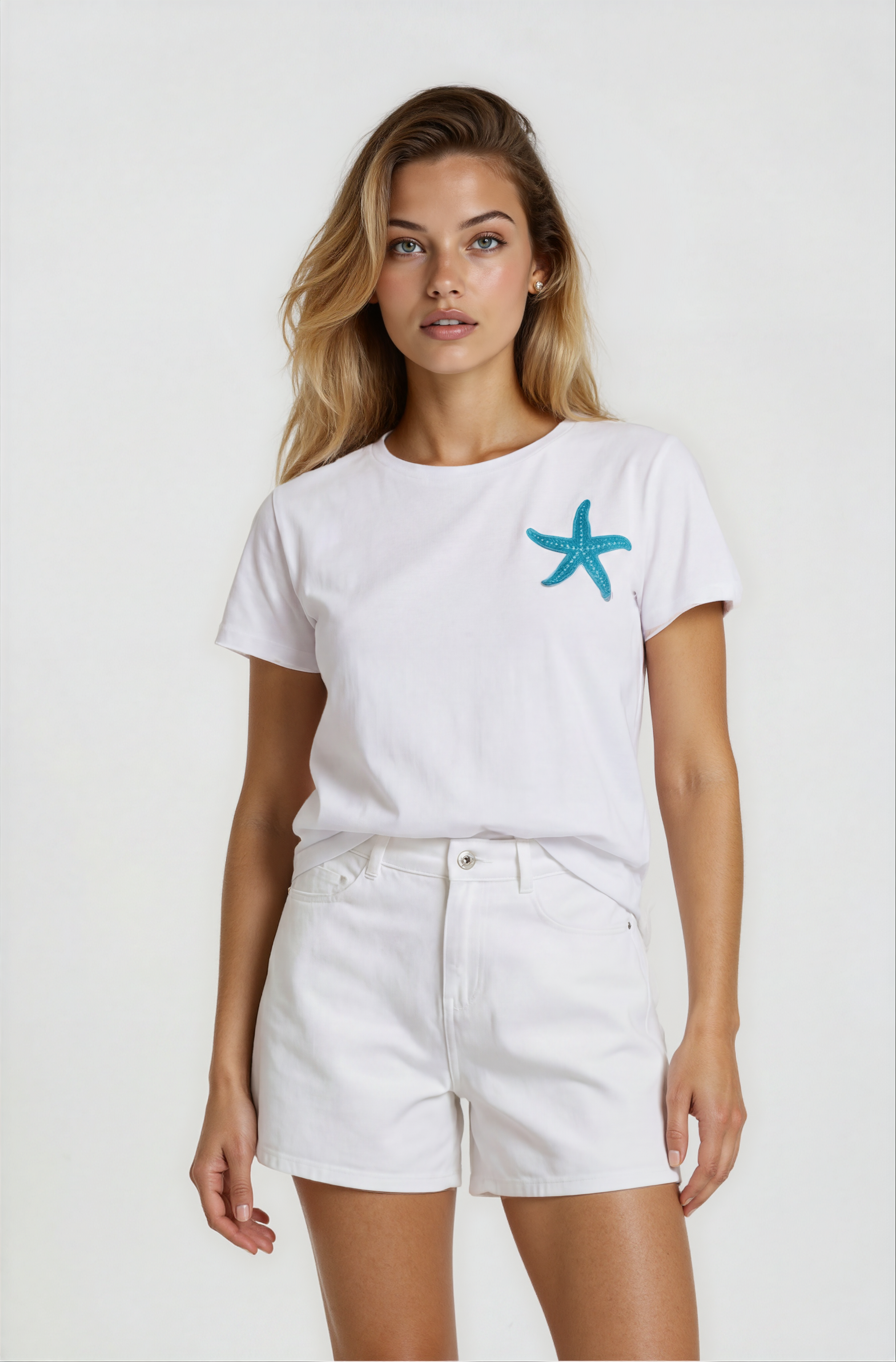 Woman wearing a white t-shirt with a blue starfish design and white shorts on a plain background